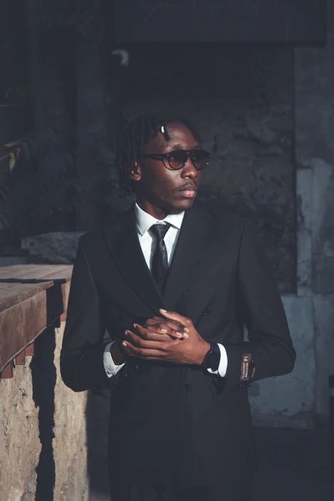 A man in a suit and sunglasses looks away.