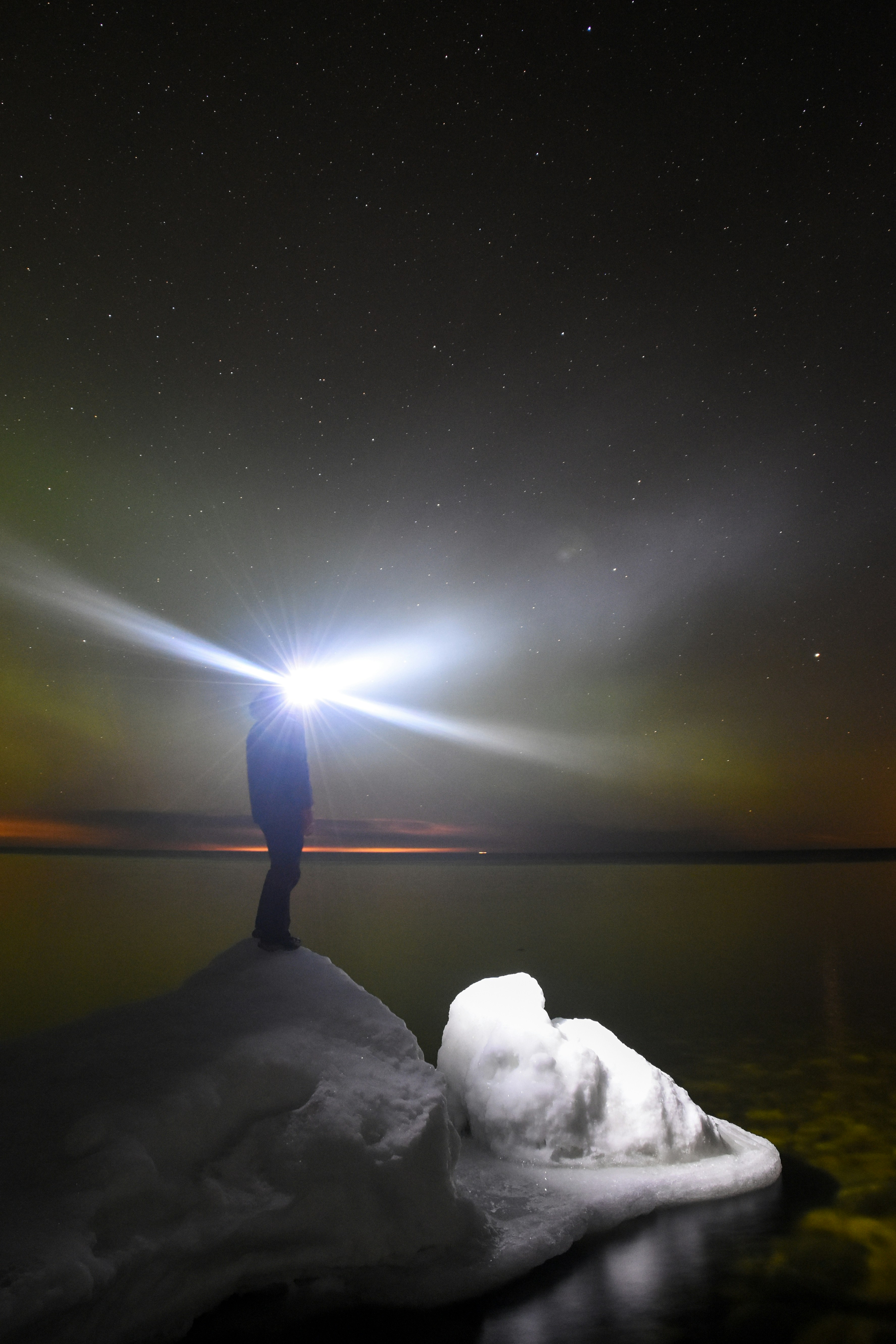 Person mit Stirnlampe steht auf Eis unter sternenklarem Himmel