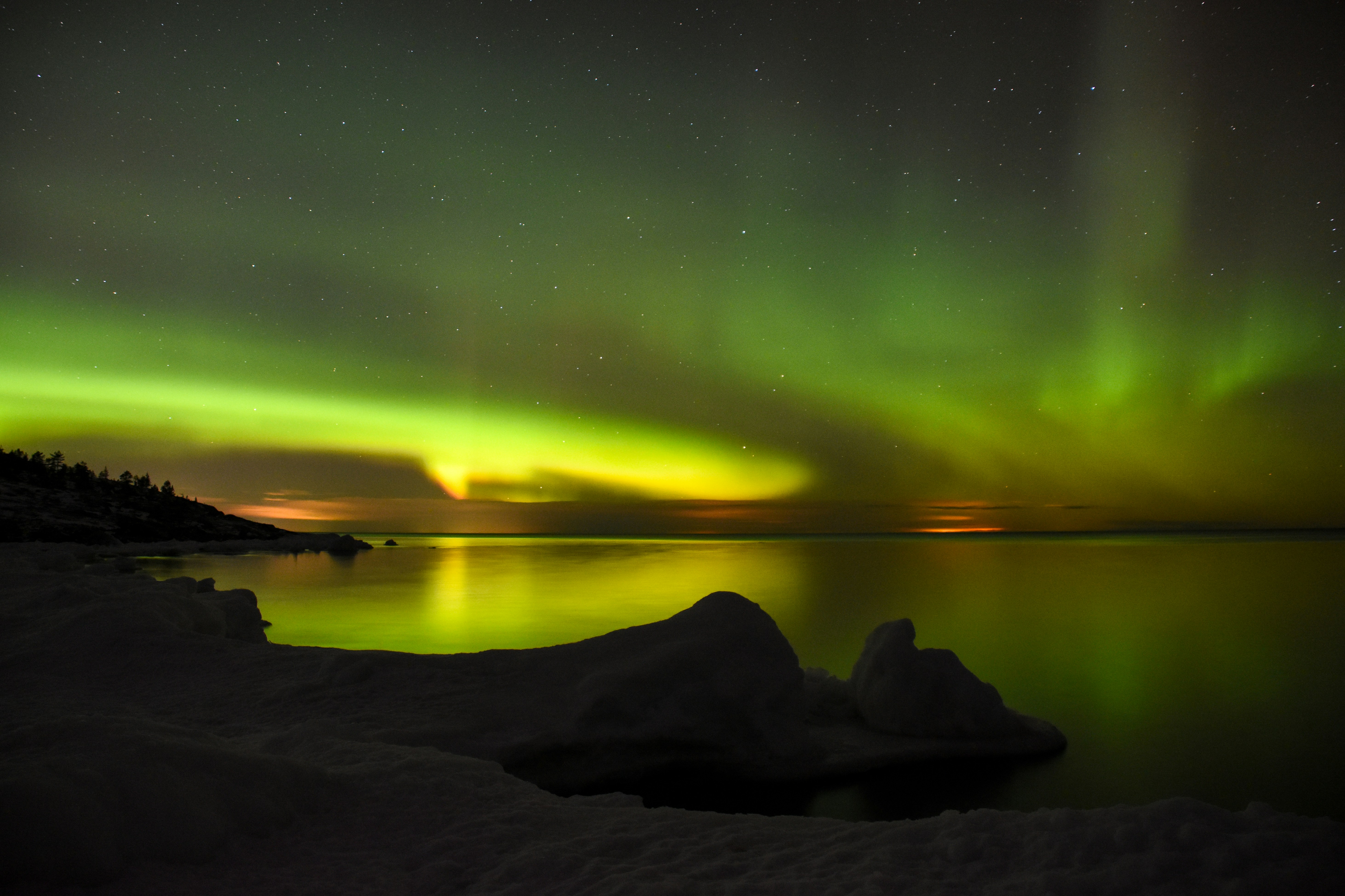Grünes Polarlicht über einem ruhigen Gewässer.