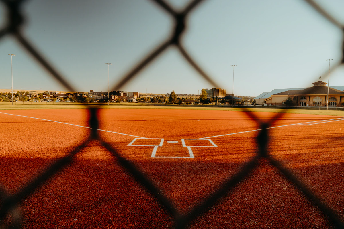 A youth baseball diamond and home plate seen through the backstop fence in late-afternoon light