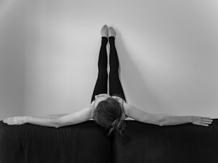 Woman with legs up wall, arms outstretched on sofa.