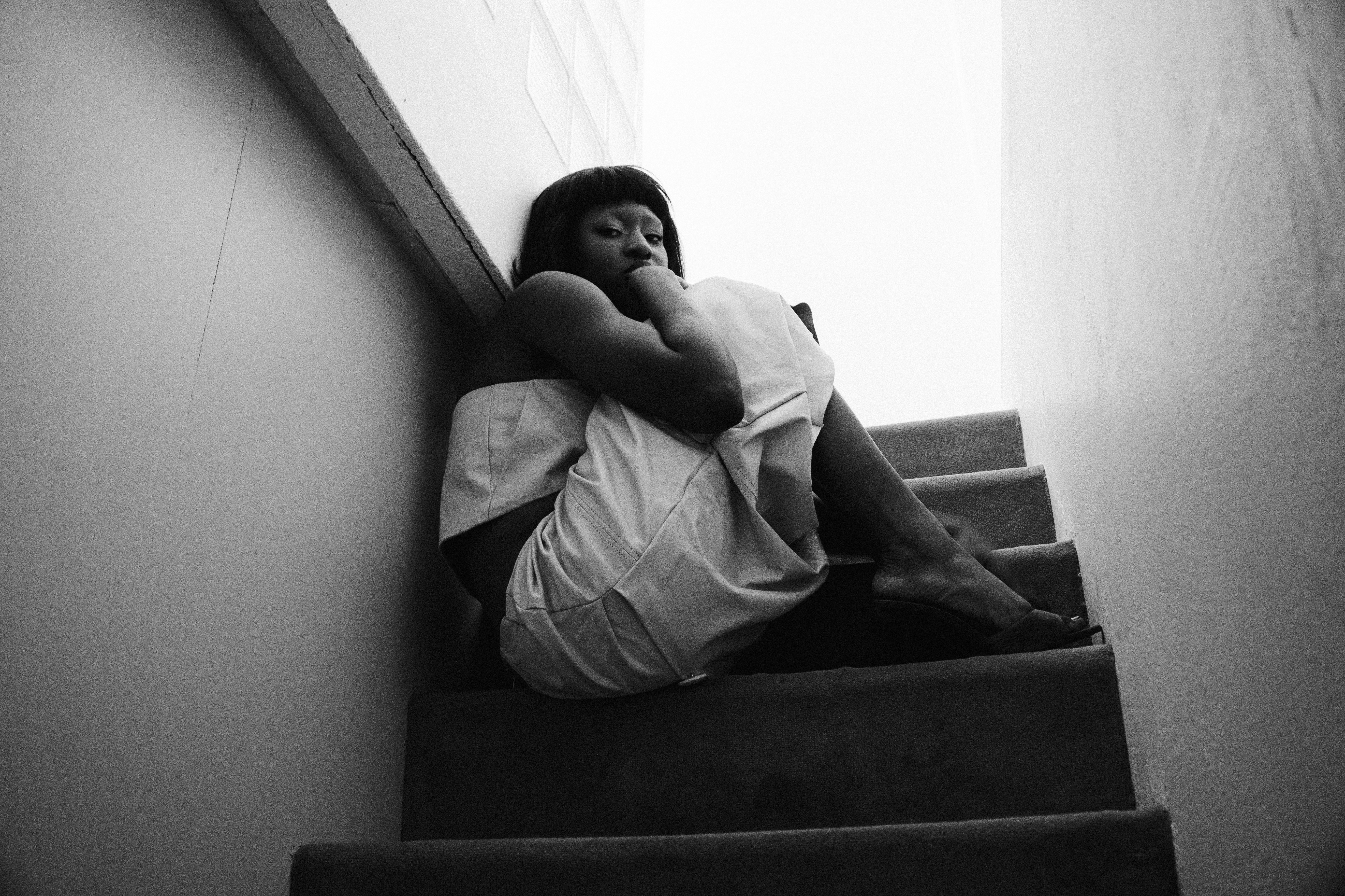 A woman sits huddled on stairs in black and white.