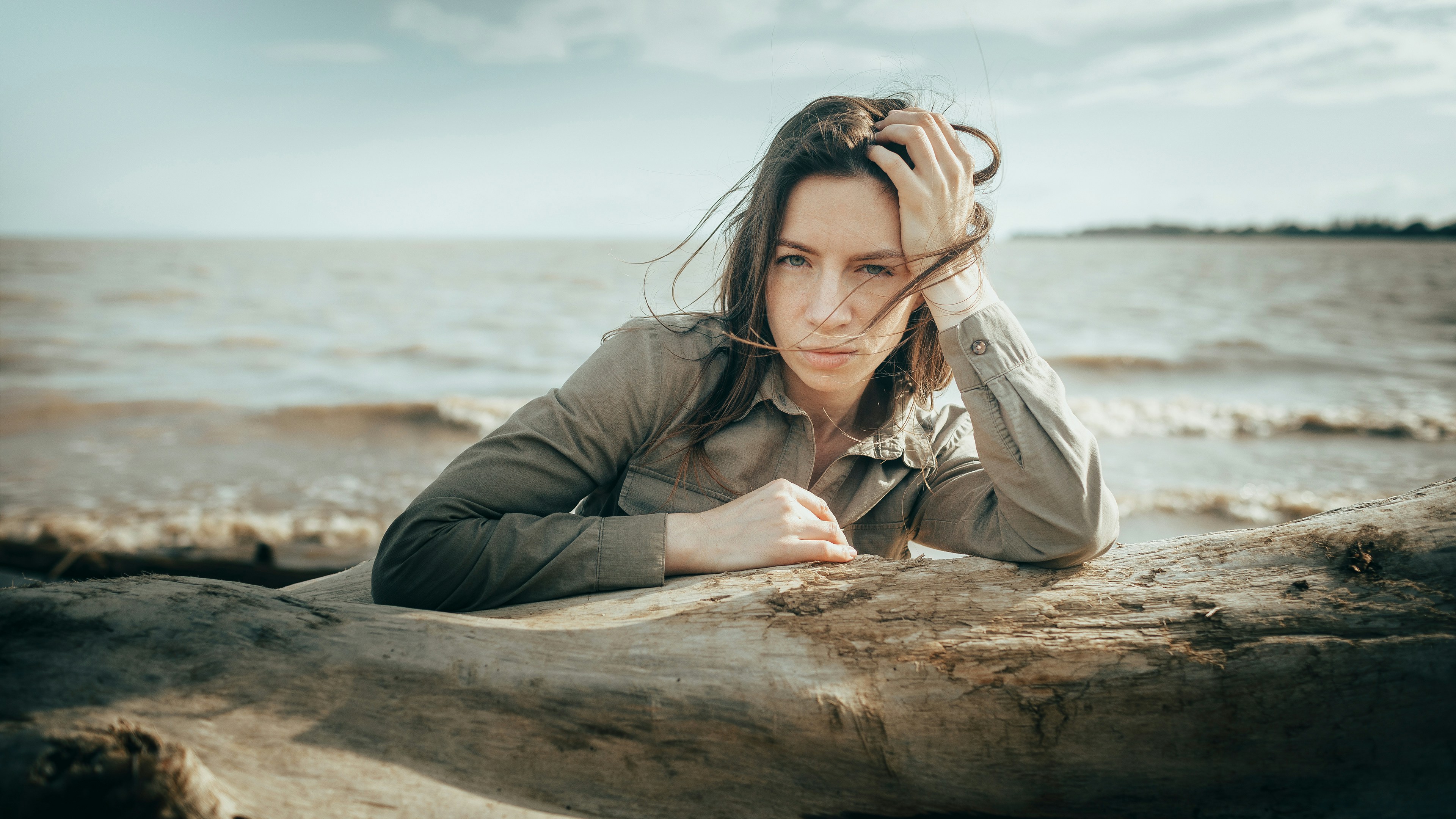 Woman rests her head on a log by the sea.