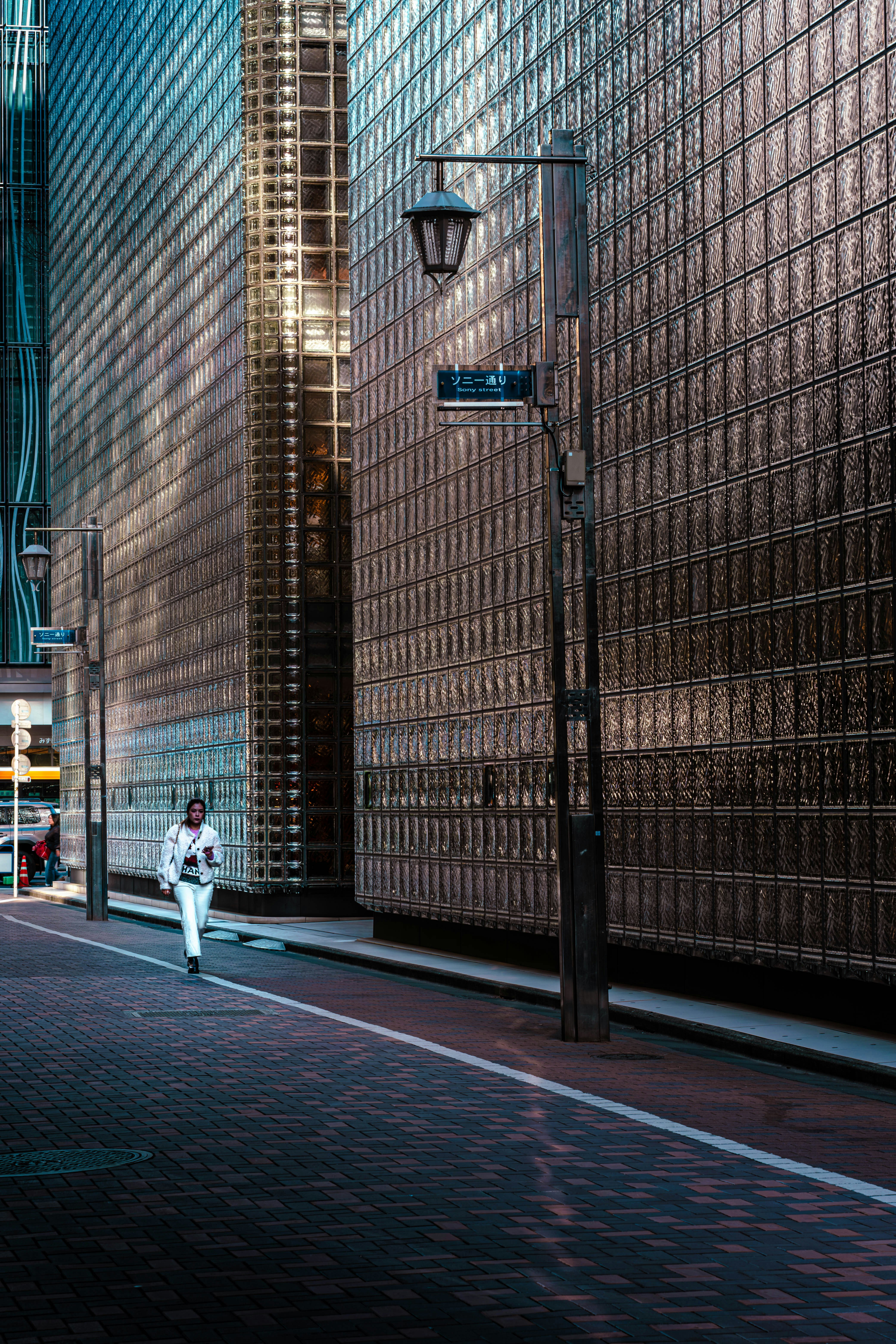 A person walks down a street between modern glass buildings.