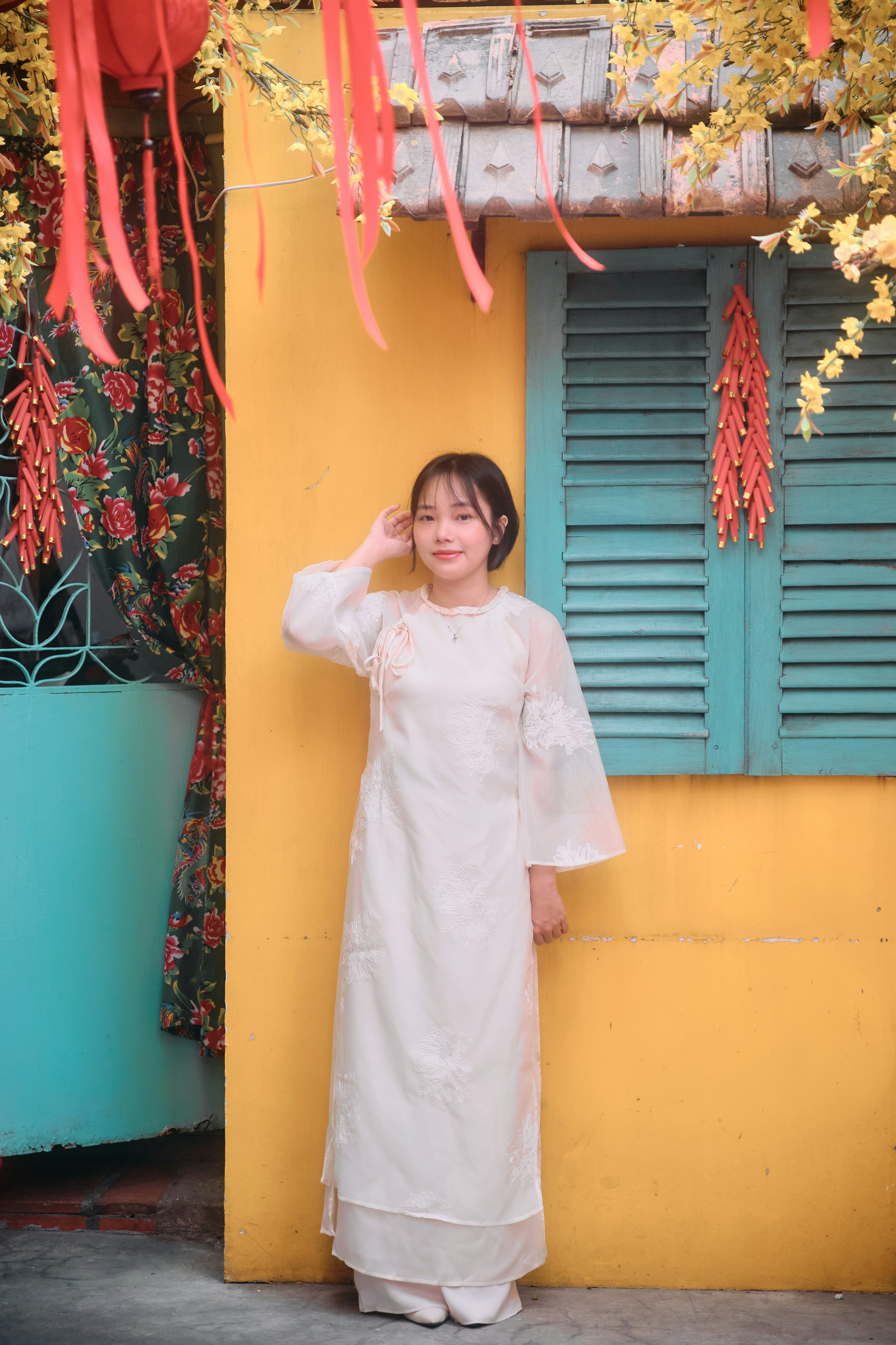 Young woman in white dress posing by yellow wall.