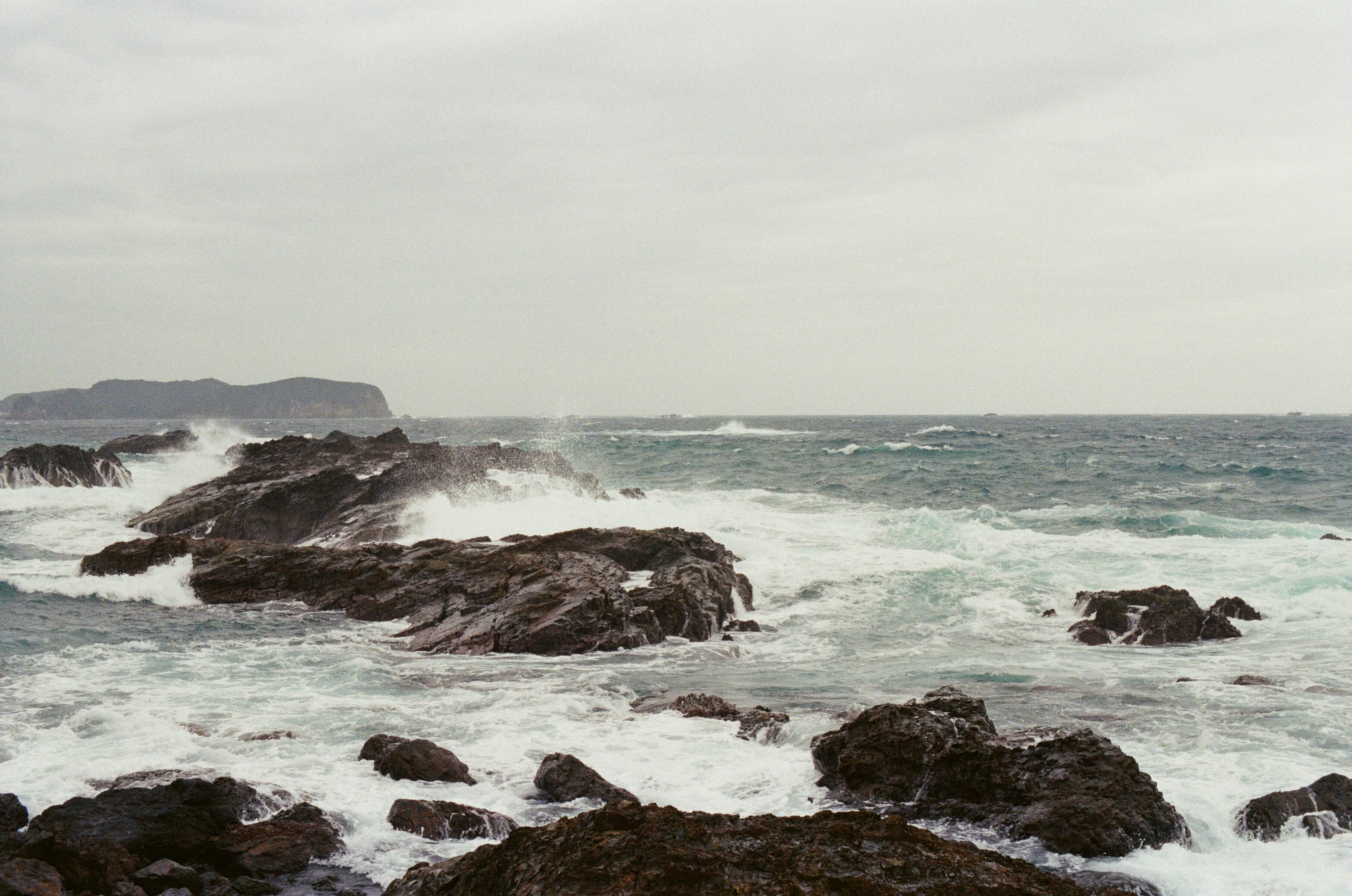 Waves crash against rocky shore under overcast sky