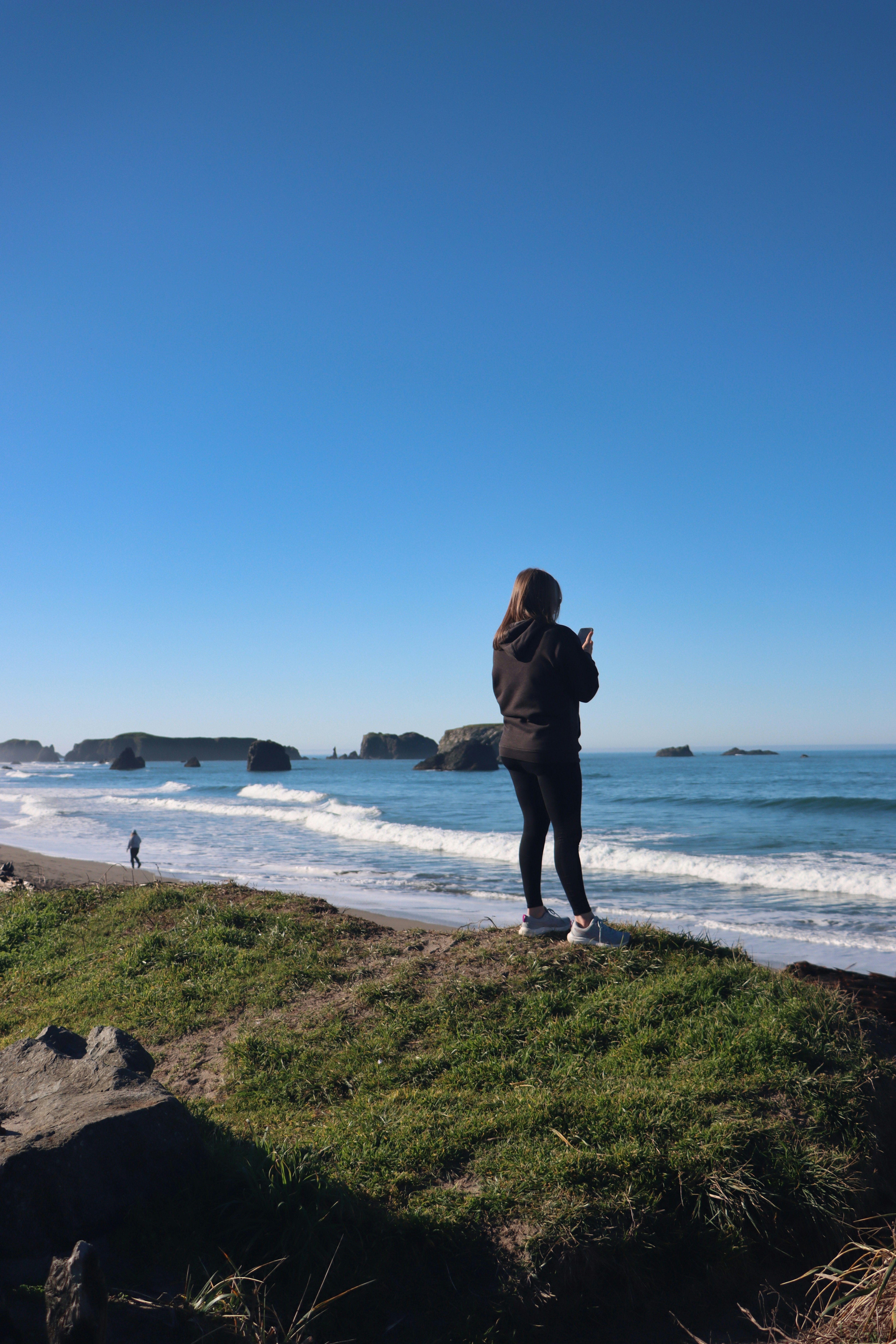 Woman standing on grassy cliff overlooking ocean waves