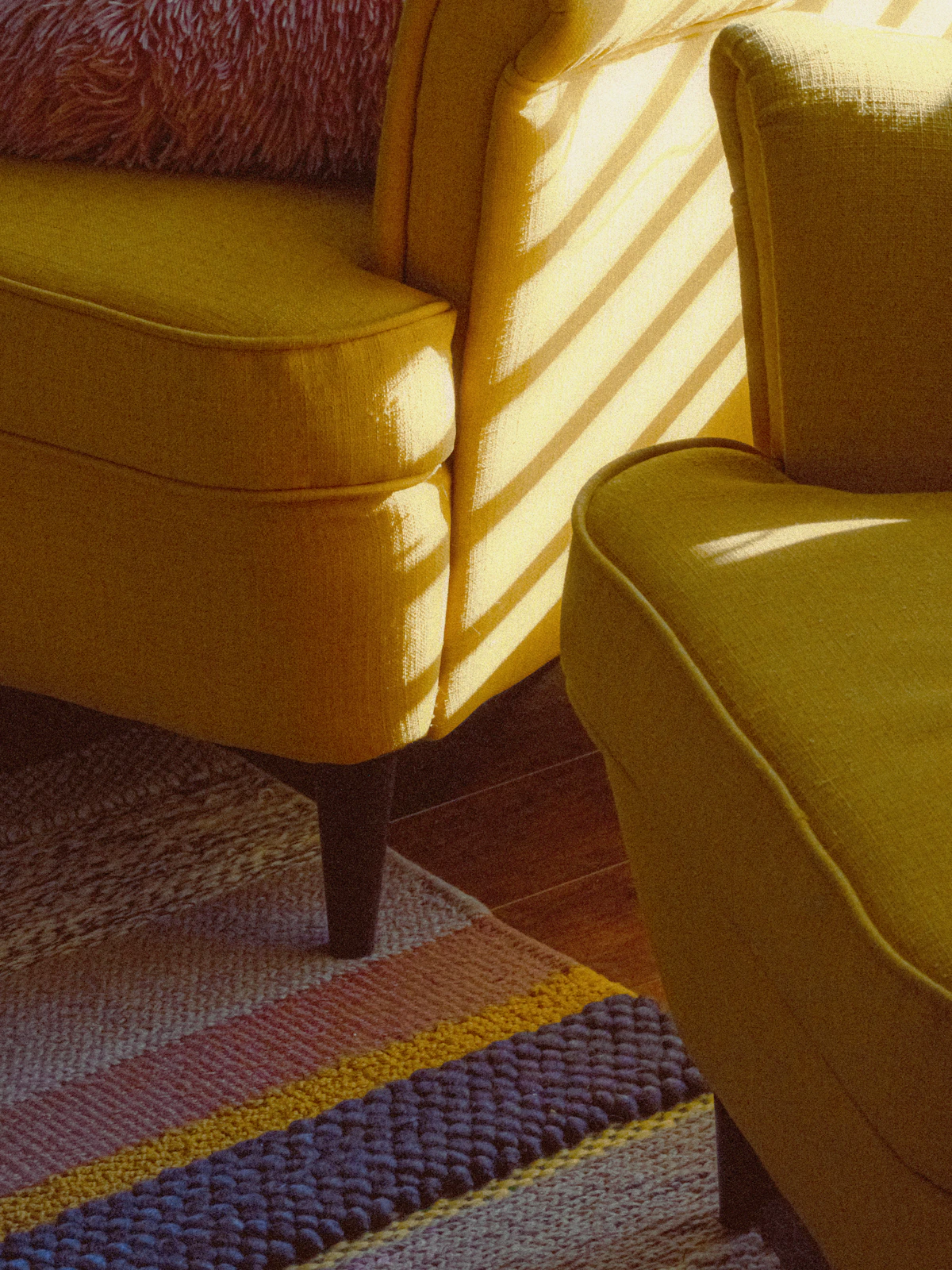 Bright living area with yellow armchairs and a striped rug catching the afternoon sun