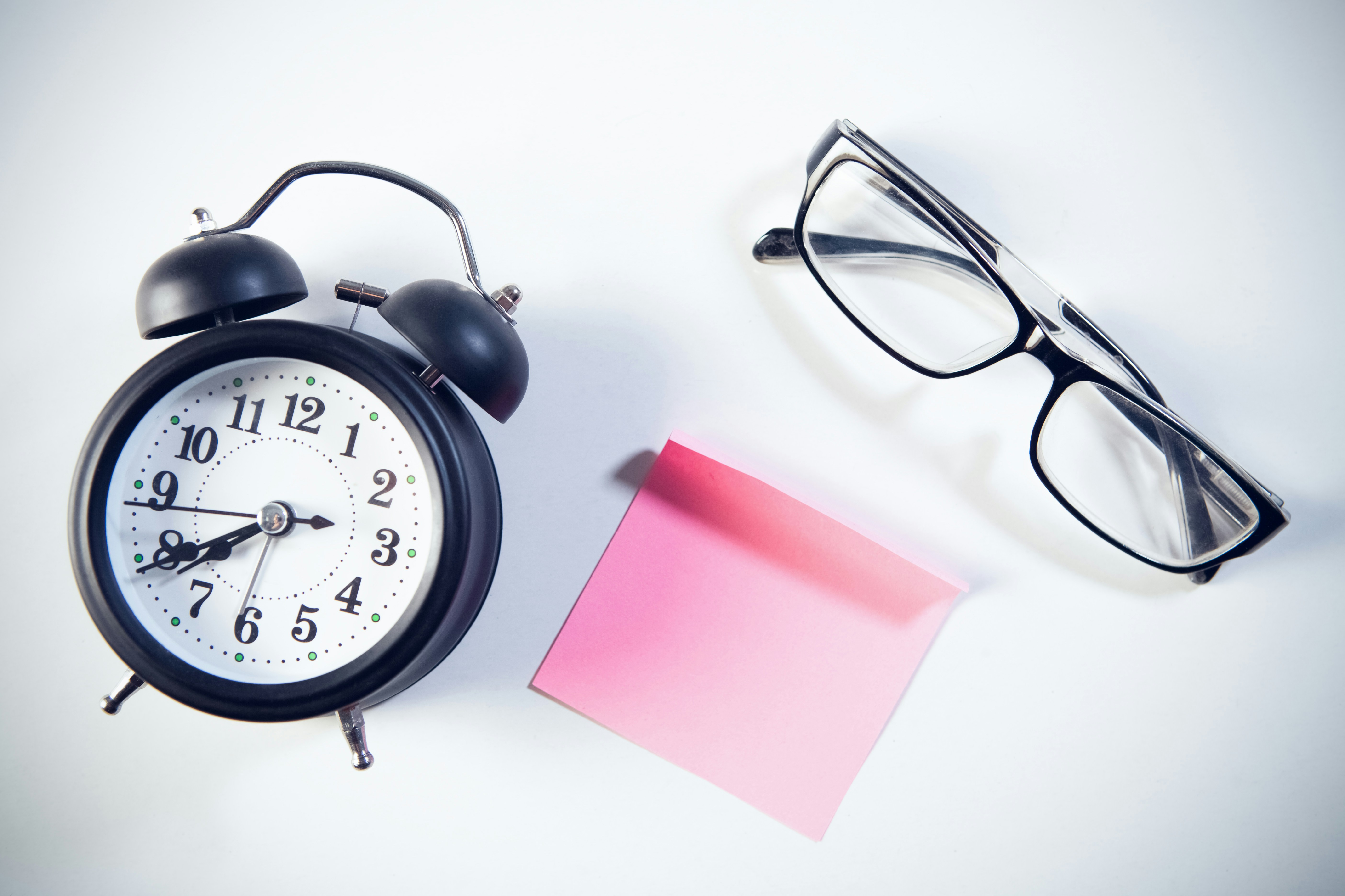 Alarm clock, eyeglasses and sticky note on white background