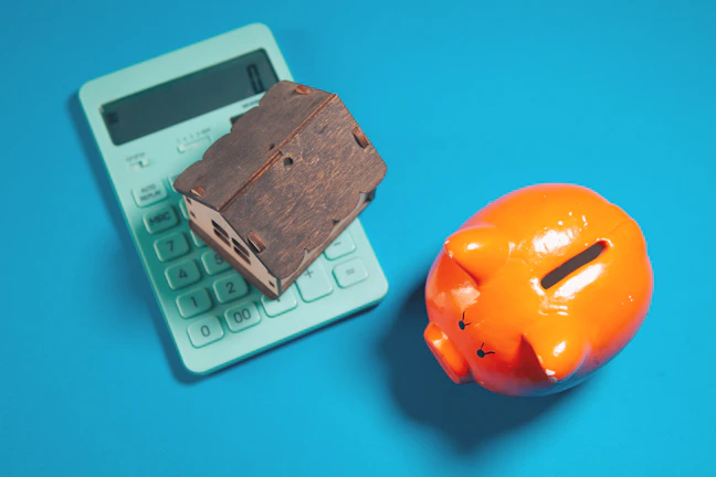 Calculator, piggy bank, and house model on blue background