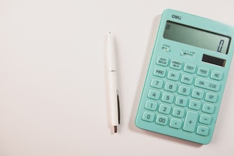A teal calculator and white pen on a white surface.