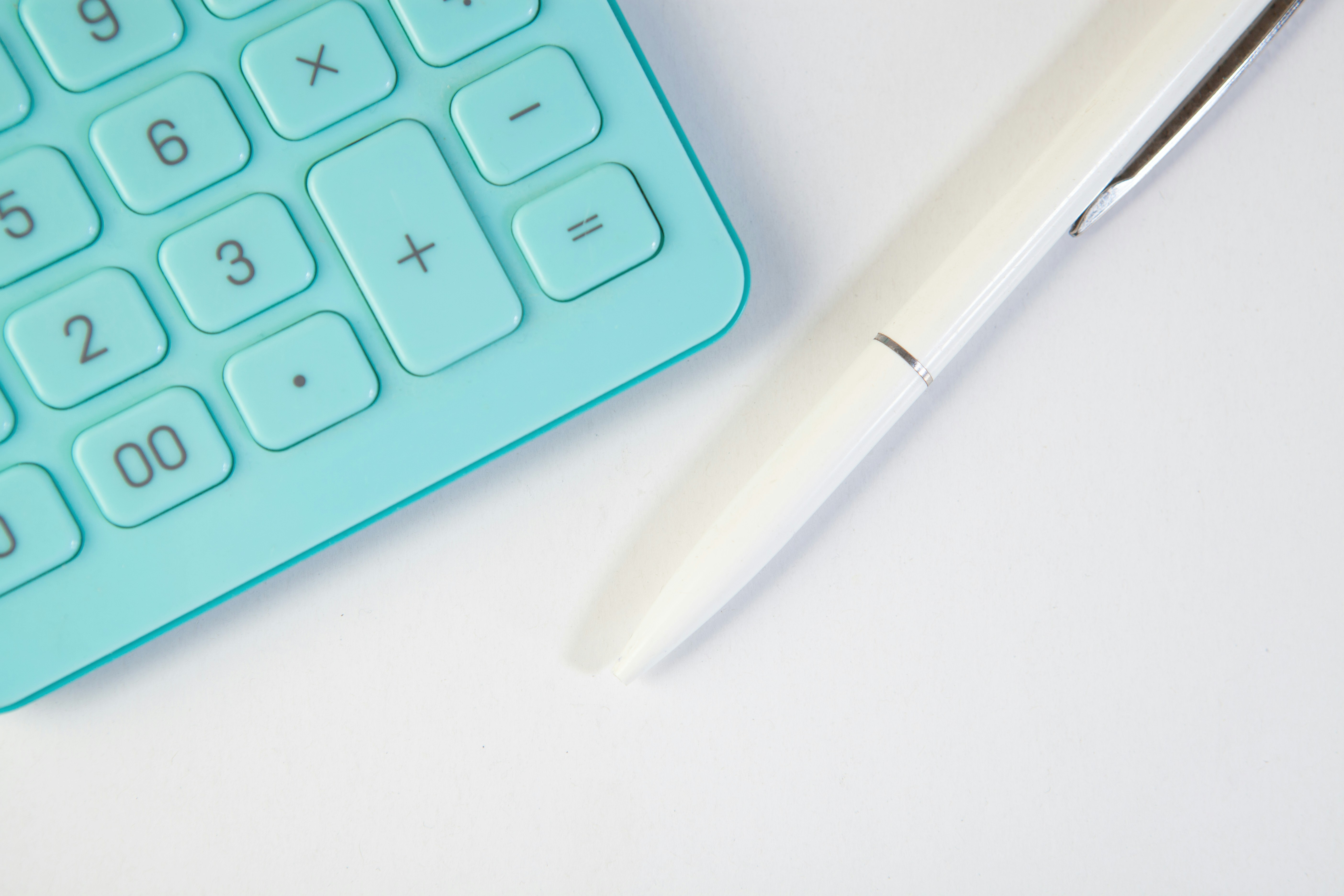 Turquoise calculator and white pen on white background
