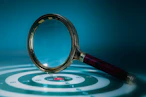 Magnifying glass over a target with bullseye.