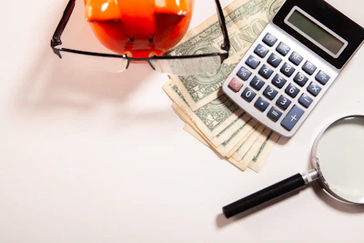 Calculator, magnifying glass, glasses, and money on white surface