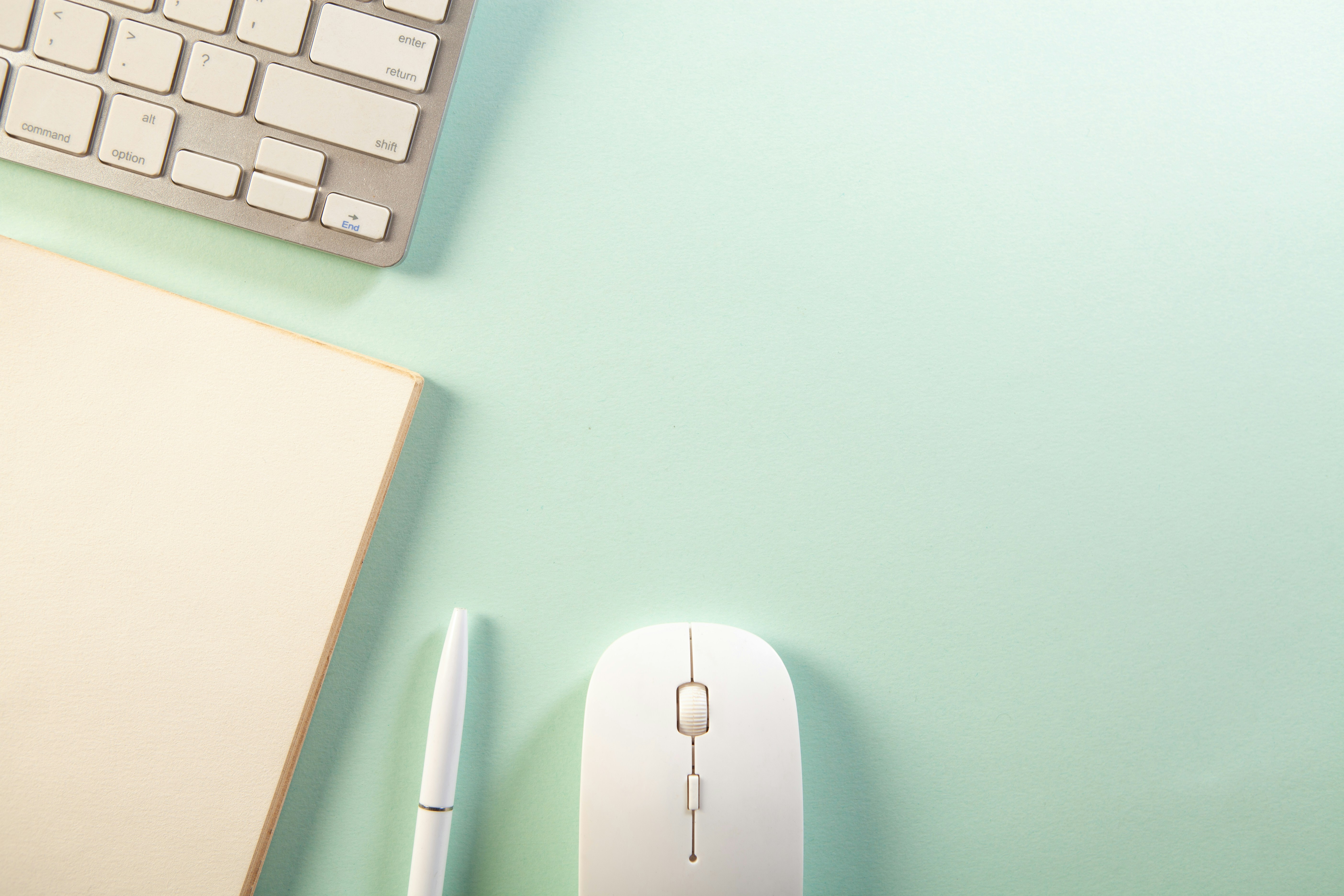 A keyboard, notebook, pen, and mouse on a desk