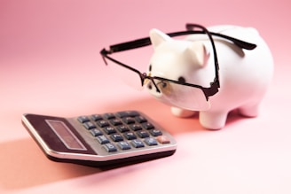 A piggy bank wearing glasses next to a calculator.