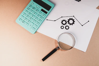 Calculator, magnifying glass, and chart with gears on paper.