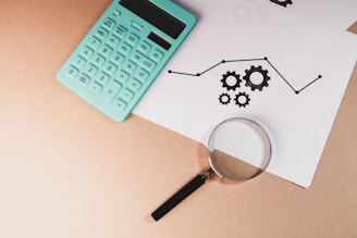 Calculator, magnifying glass, and chart with gears on paper.