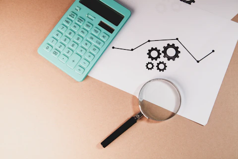 Calculator, magnifying glass, and chart with gears on paper.