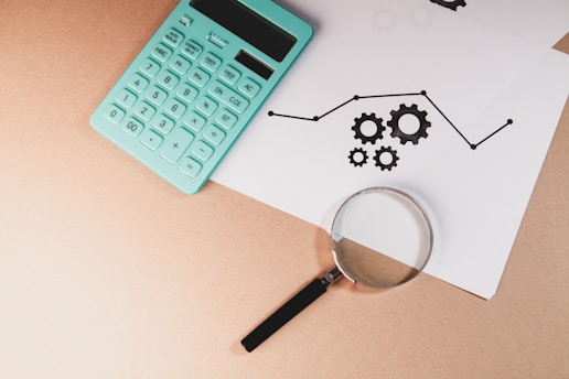 Calculator, magnifying glass, and chart with gears on paper.