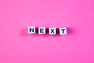 White letter beads spell out next on pink background