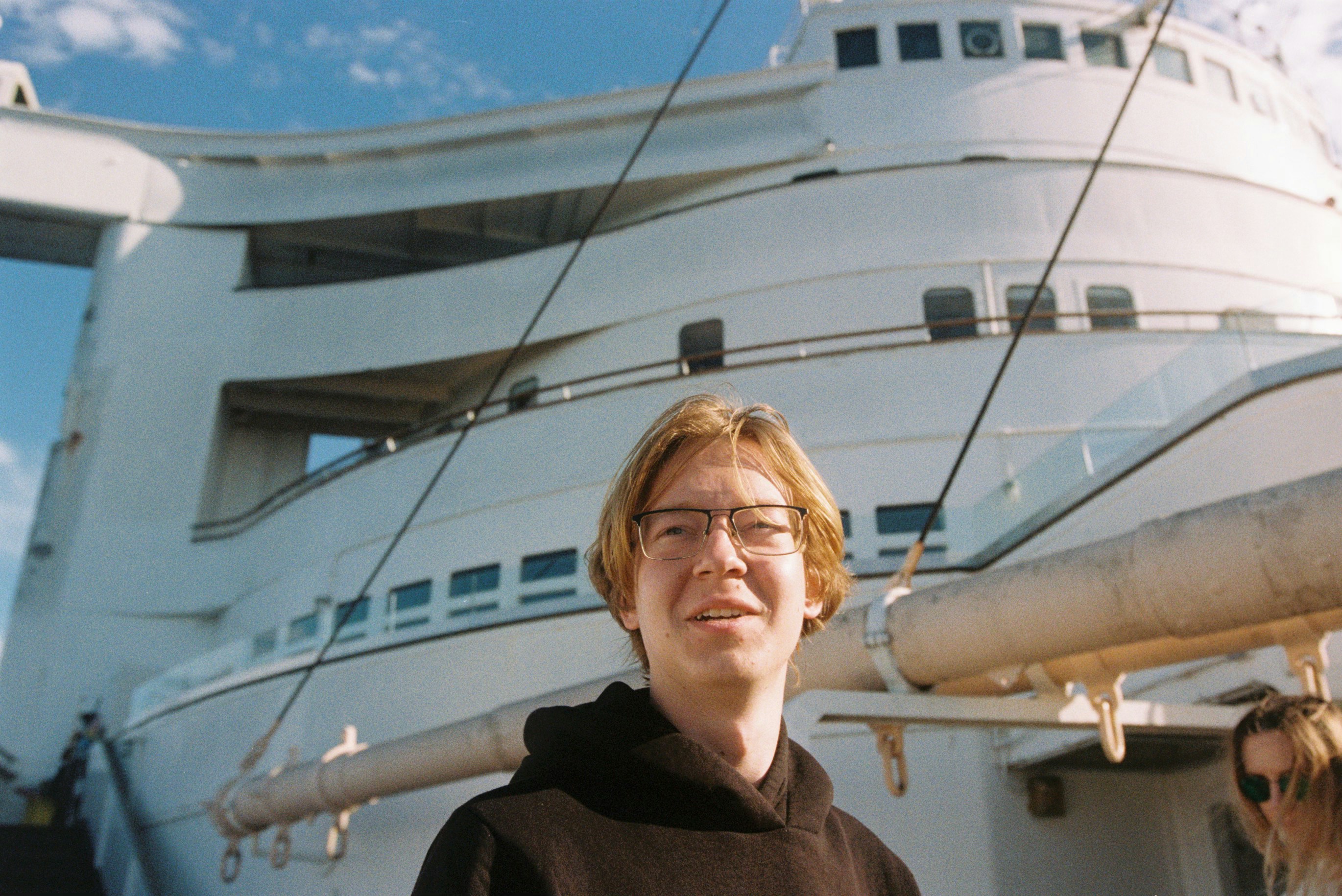 Un joven con gafas está frente a un gran barco blanco.
