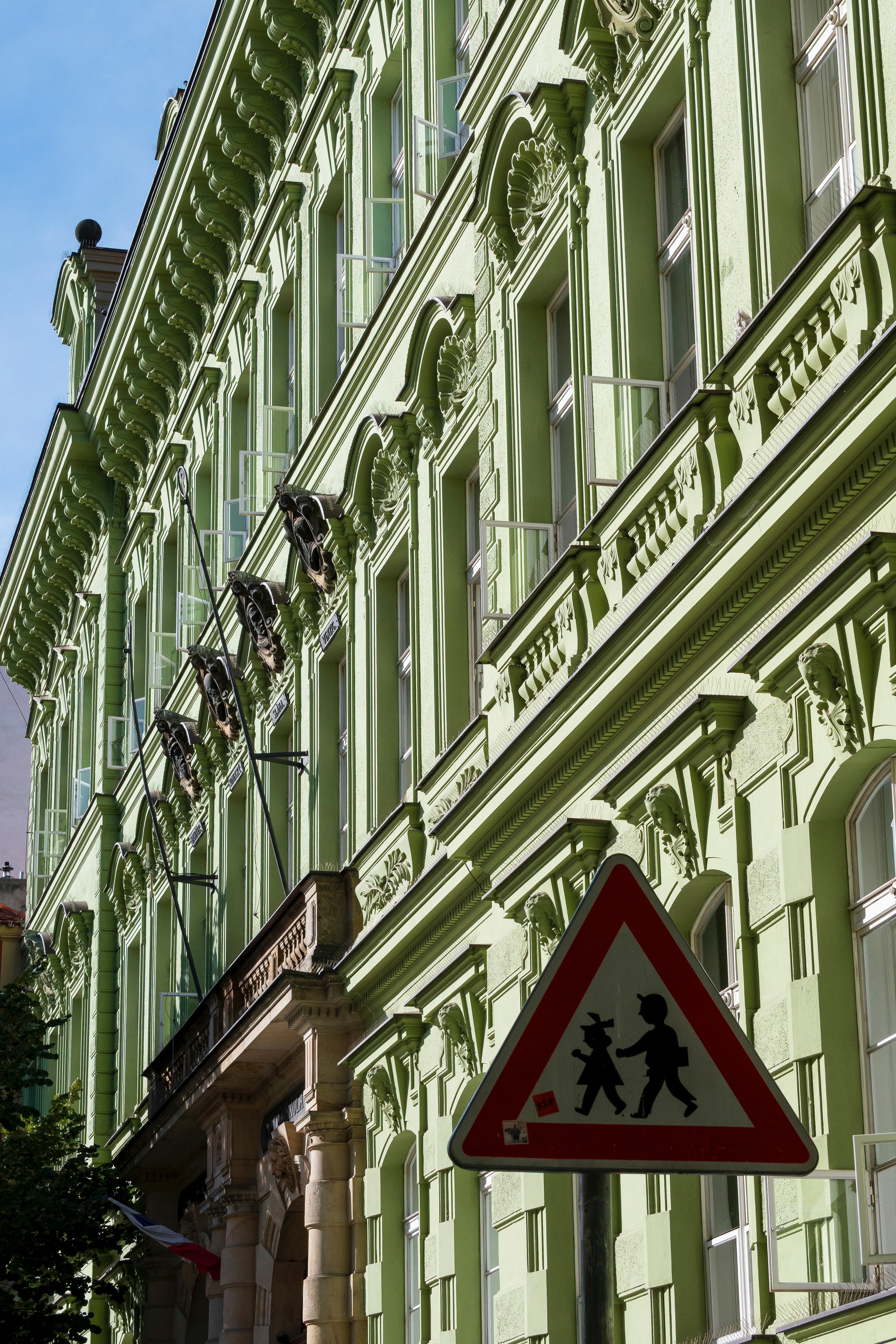 Green building facade with a pedestrian crossing sign.