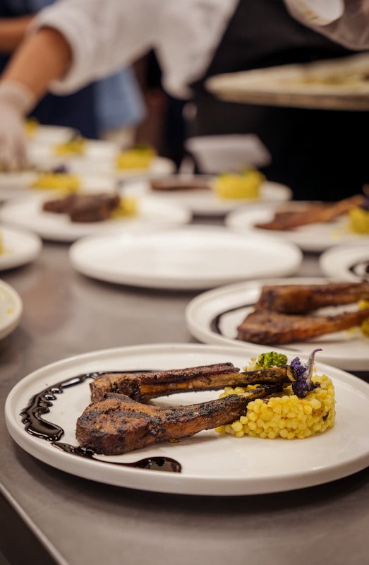 Chef plates grilled lamb chops with couscous and garnish, final touch.