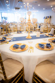 Elegant table setting with gold chairs and blue napkins.