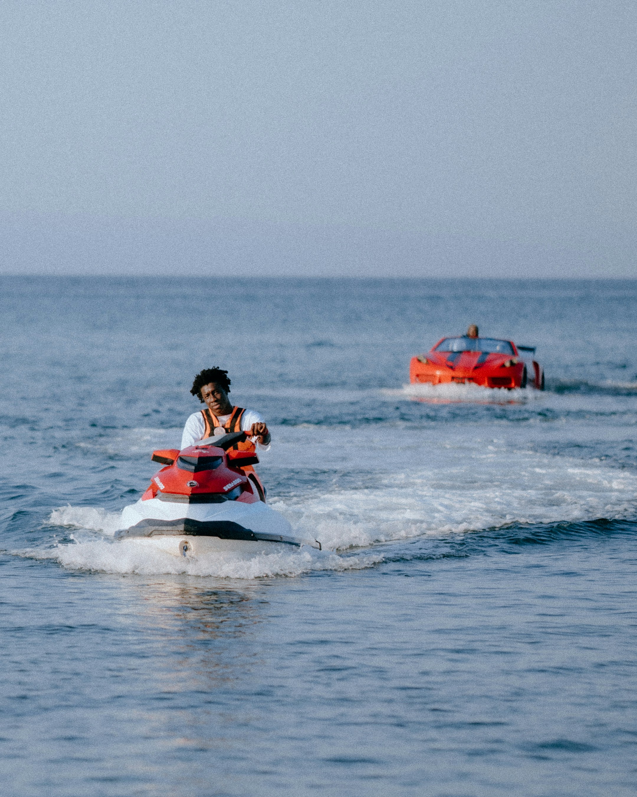 Man riding jet ski with red car in background