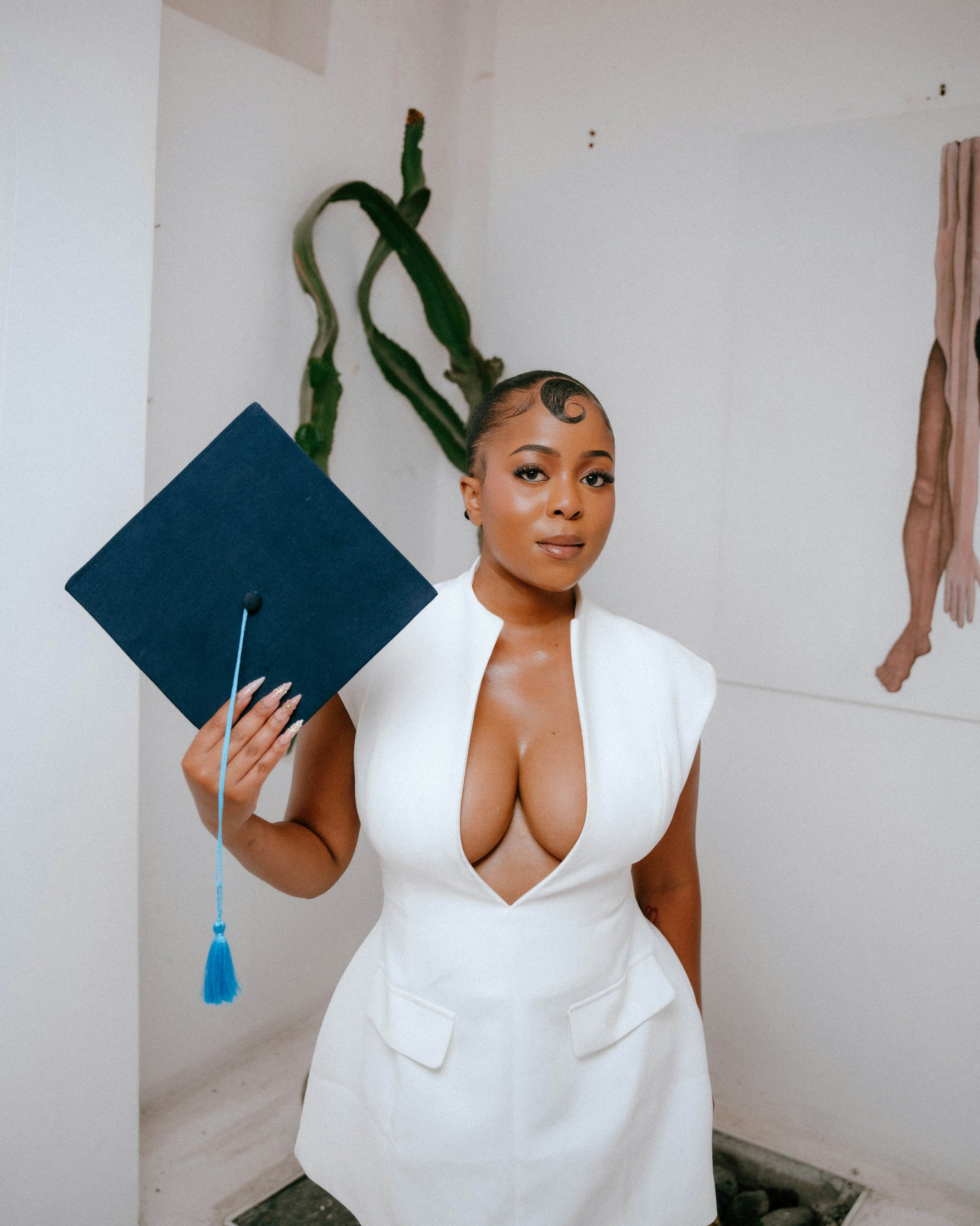 Una mujer con vestido blanco sostiene una gorra de graduación.