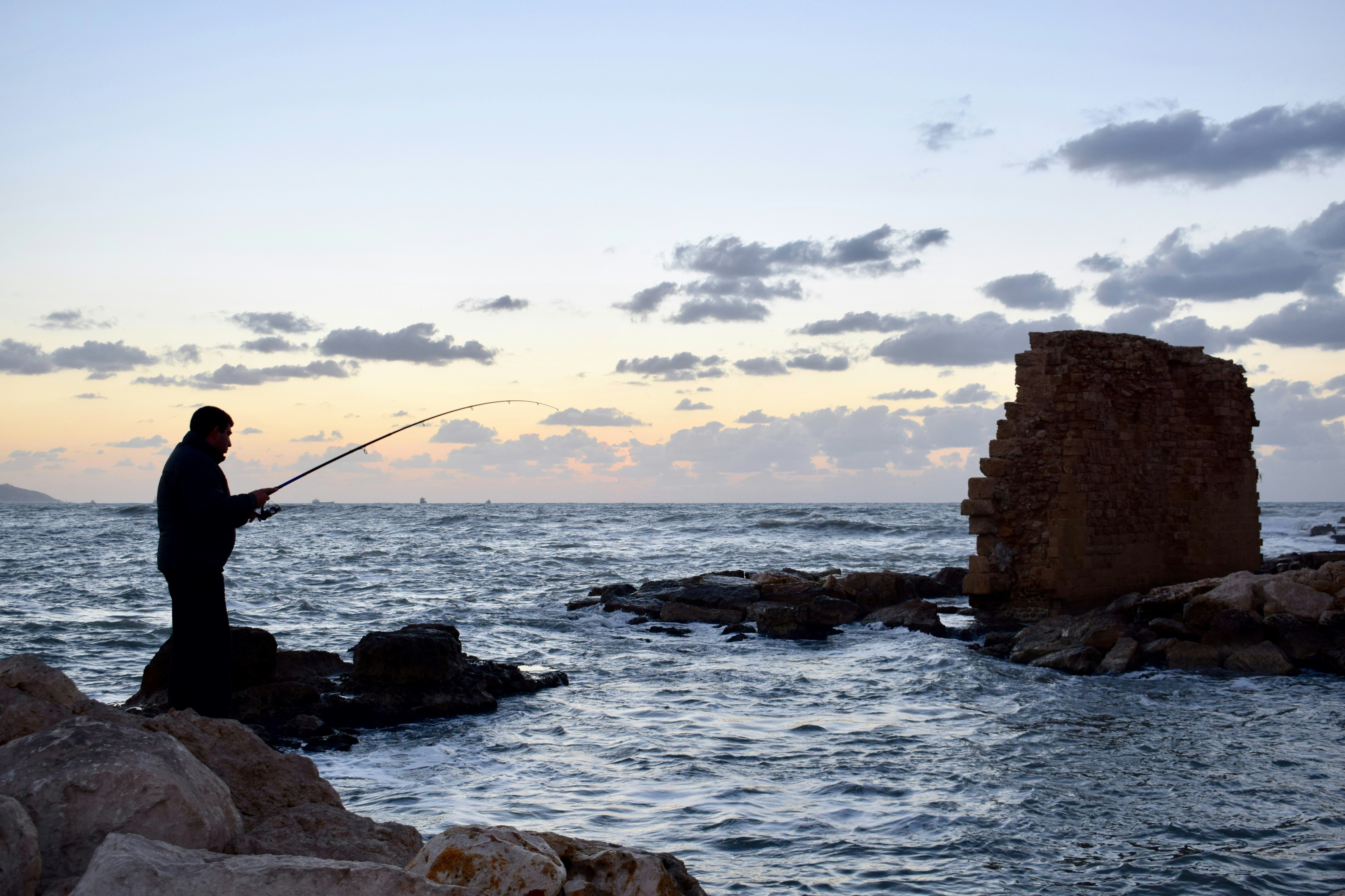 Pescador lanza línea cerca de una torre antigua al anochecer
