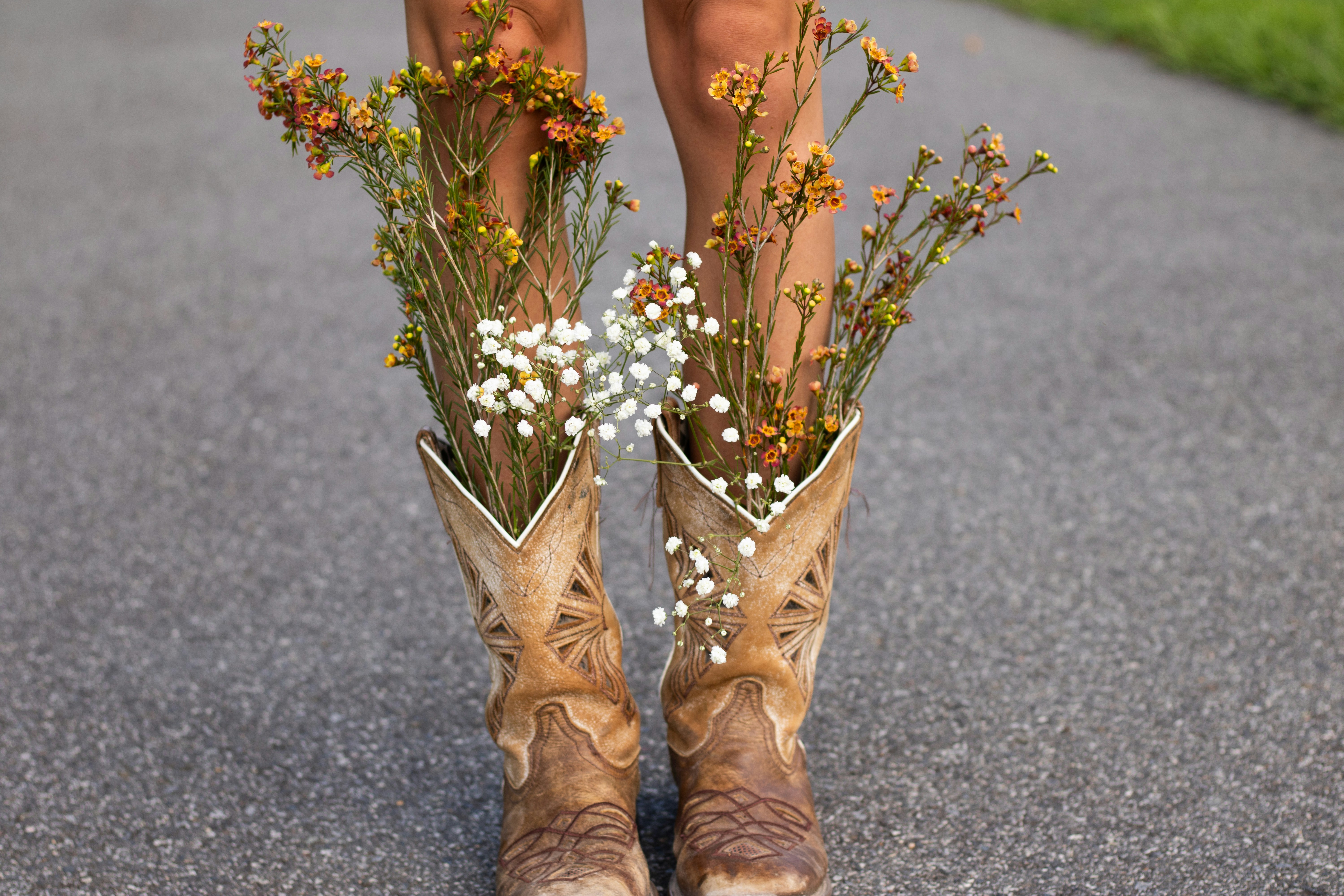 Cowboy boots filled with wildflowers on a paved surface.