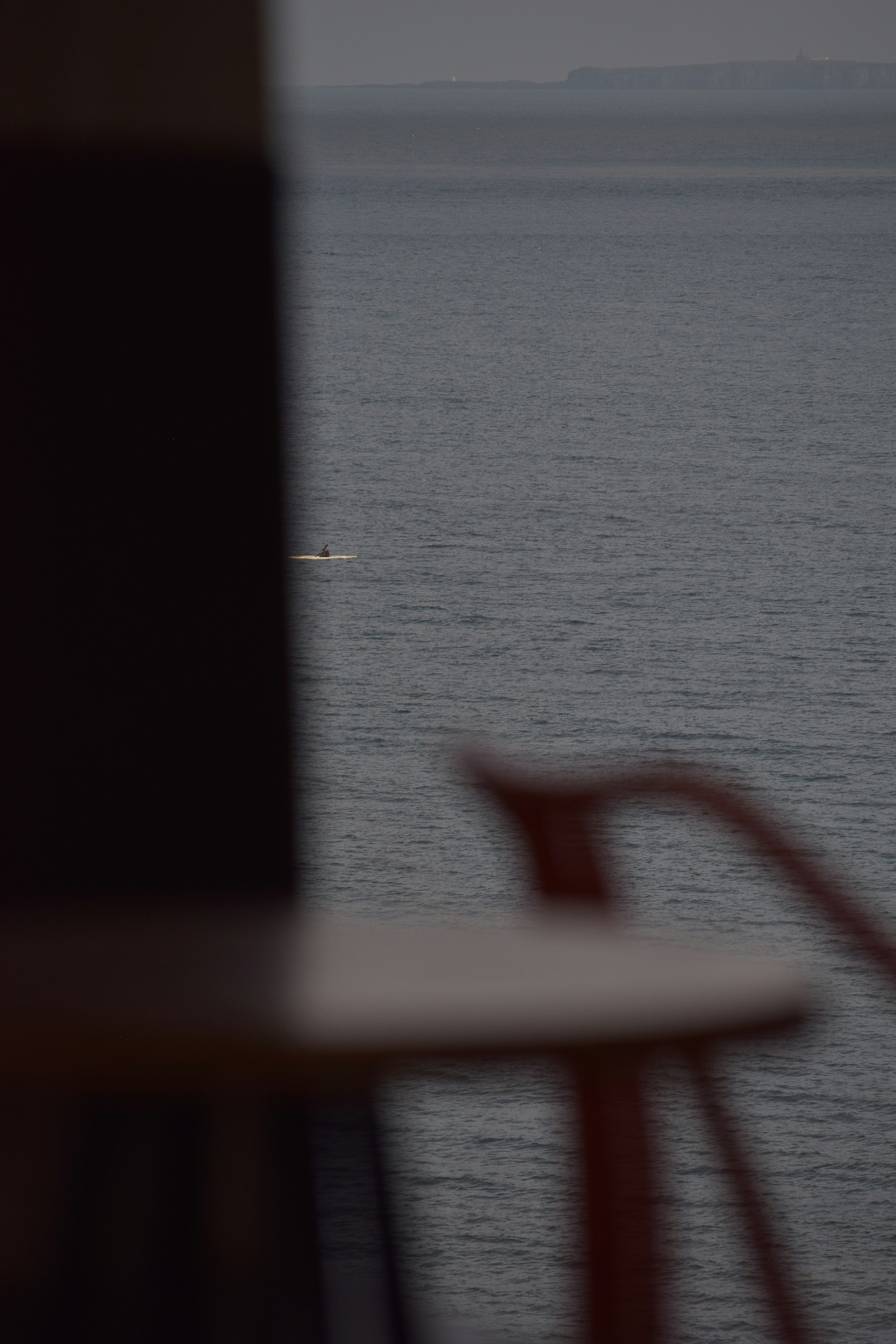 A lone kayaker paddles on a calm, gray sea.