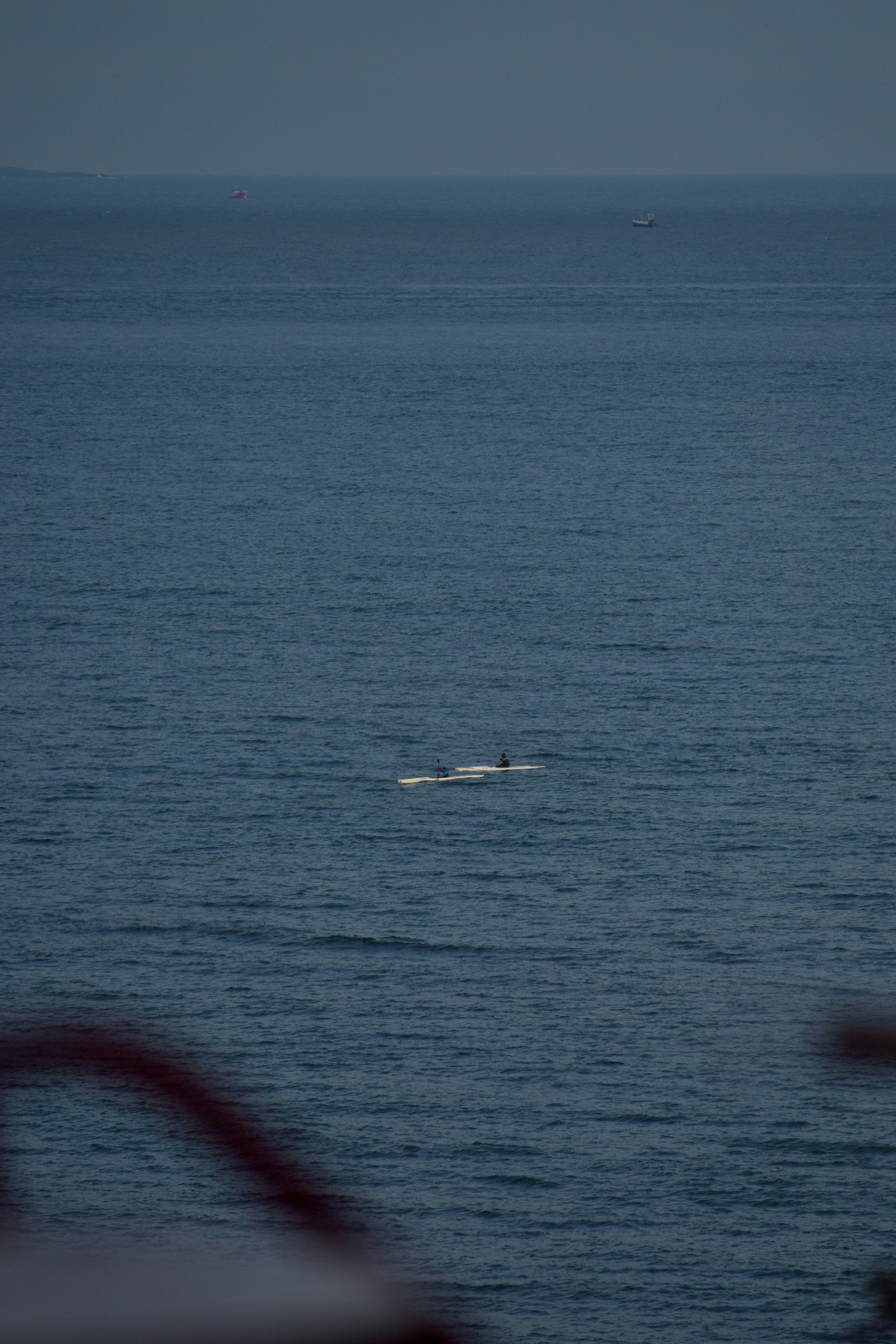 Two people paddle a canoe on a calm blue ocean.