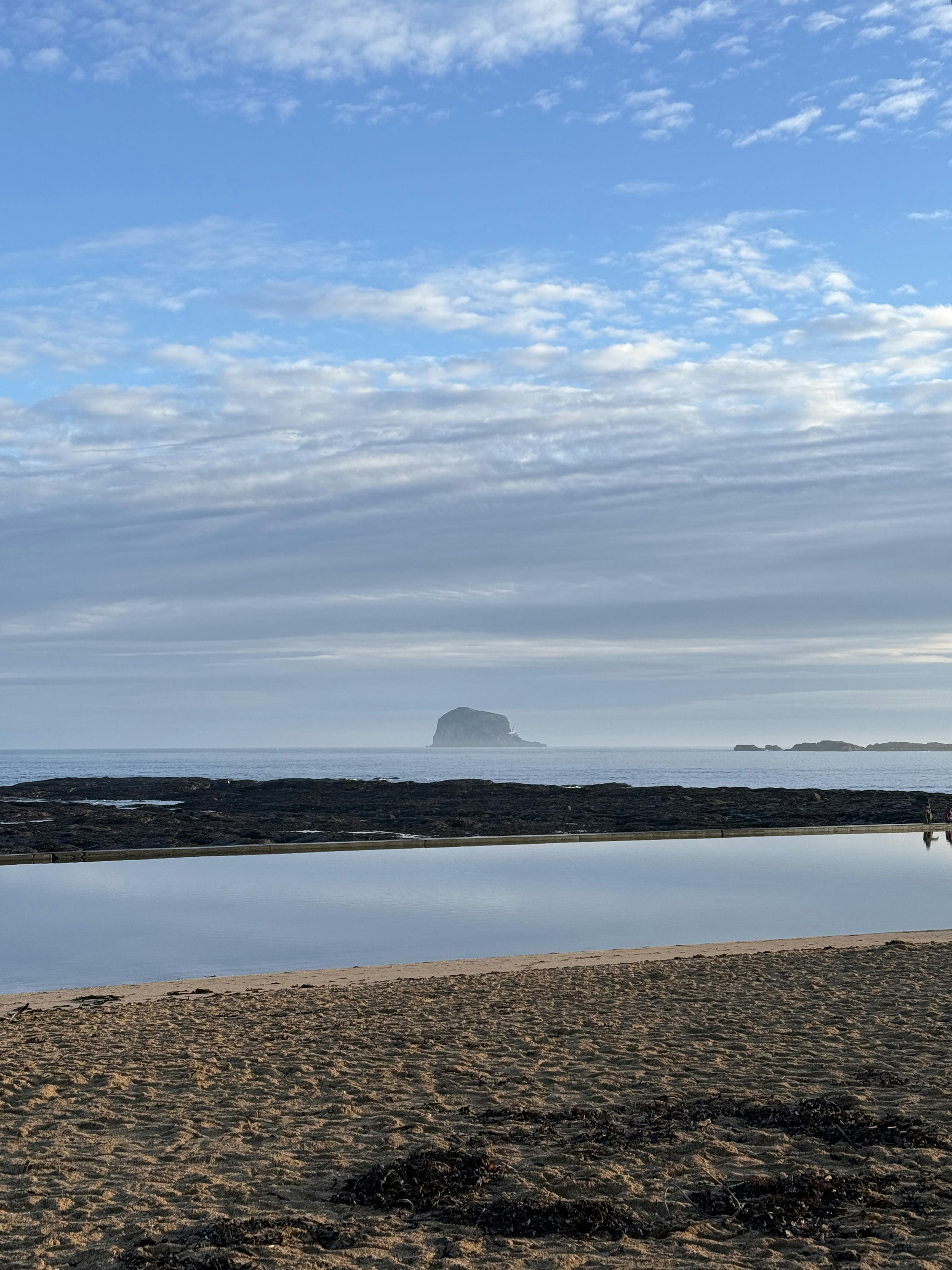 Calm ocean with a distant island under a cloudy sky.