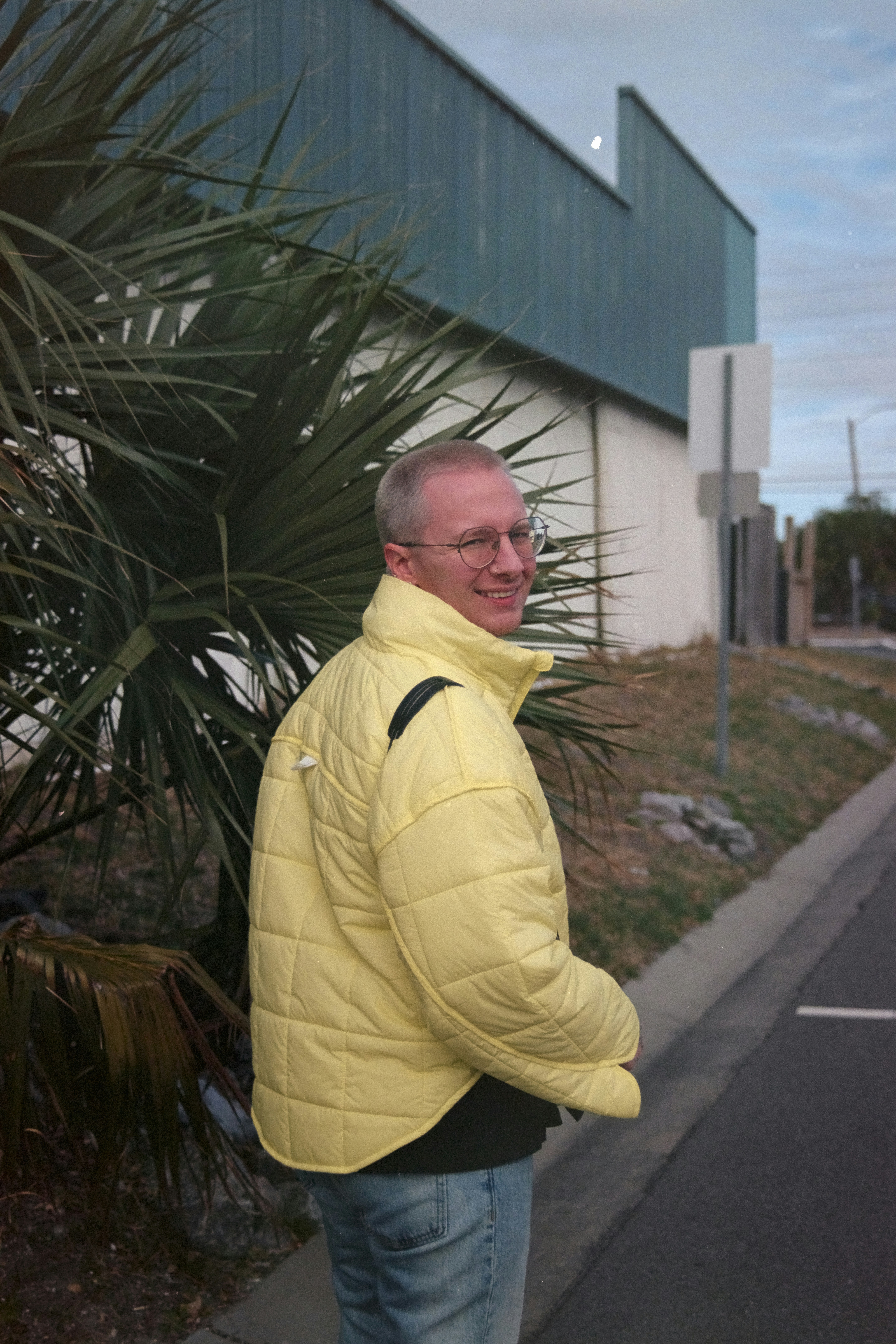 Uomo con la giacca gialla passa accanto a una palma e un edificio