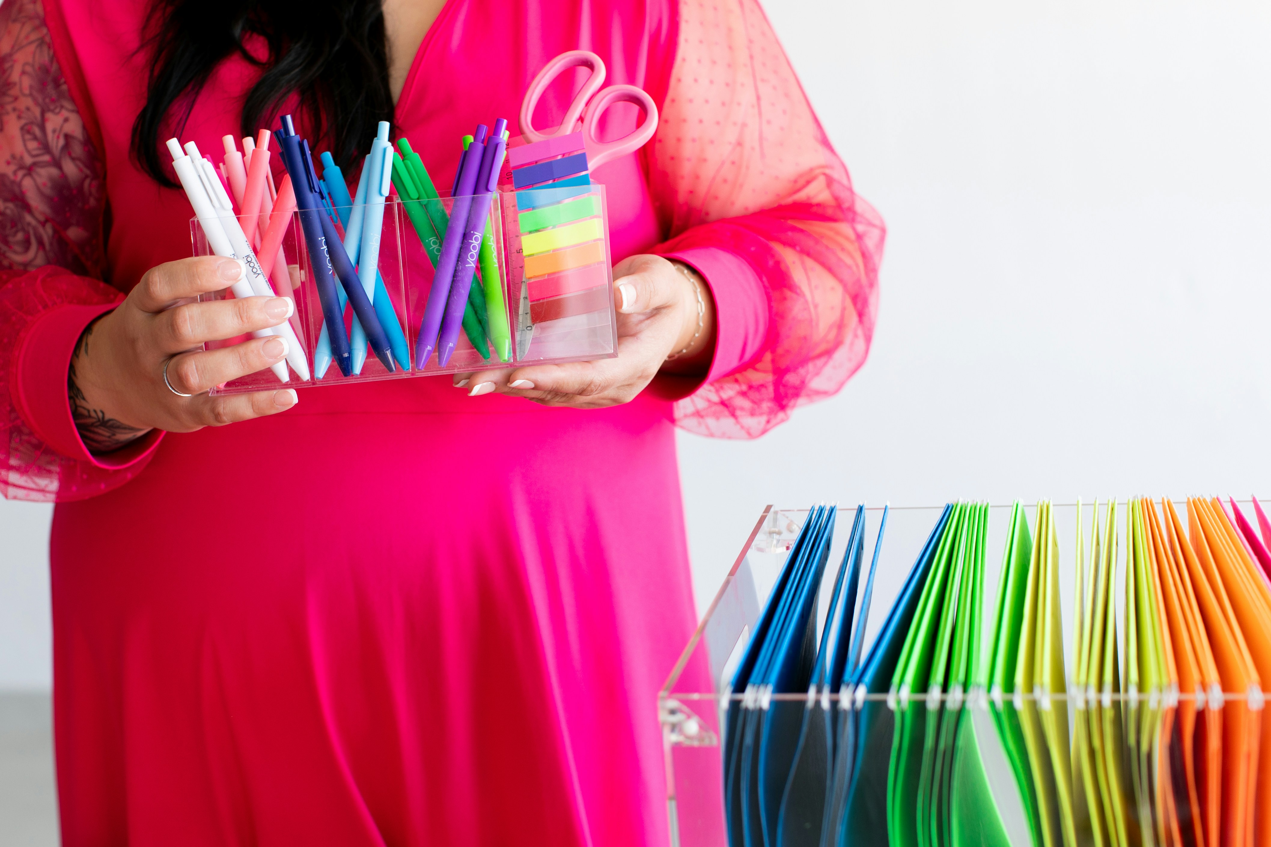 Woman in pink dress holding colorful pens and scissors.