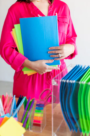 Woman in pink holding colorful files and office supplies