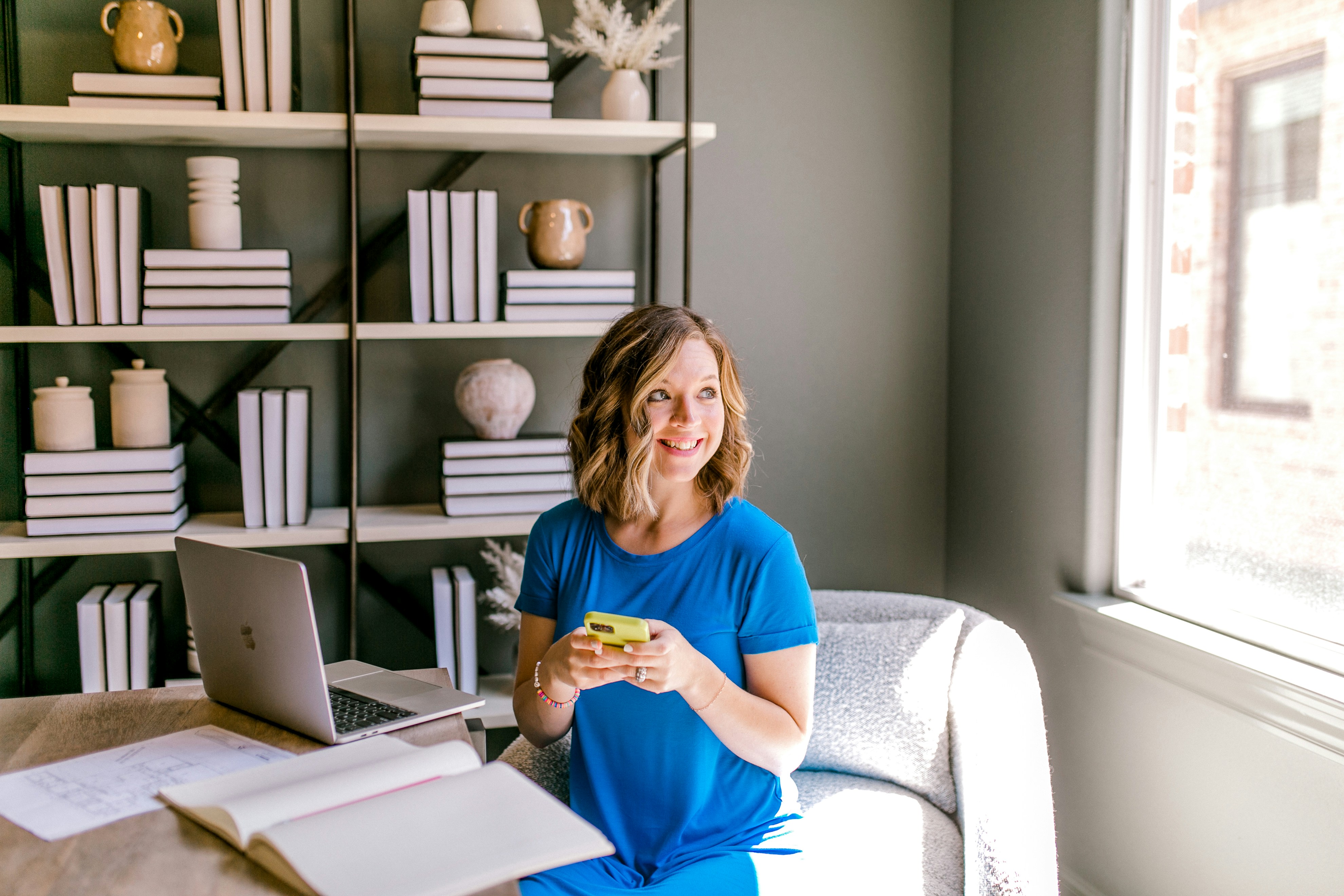 Femme en robe bleue assise au bureau avec un ordinateur portable.