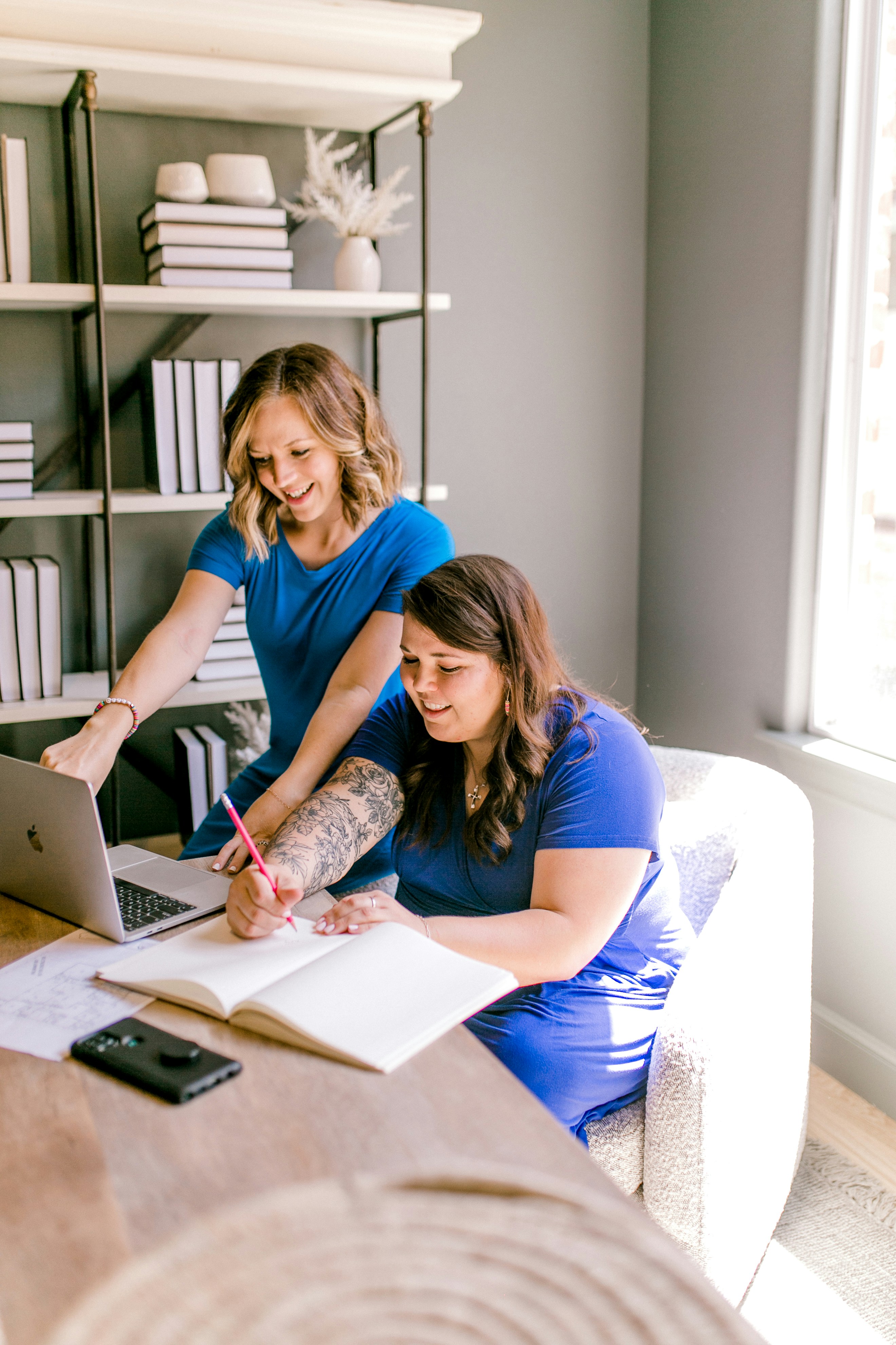 Two women working together on a laptop and notebook.