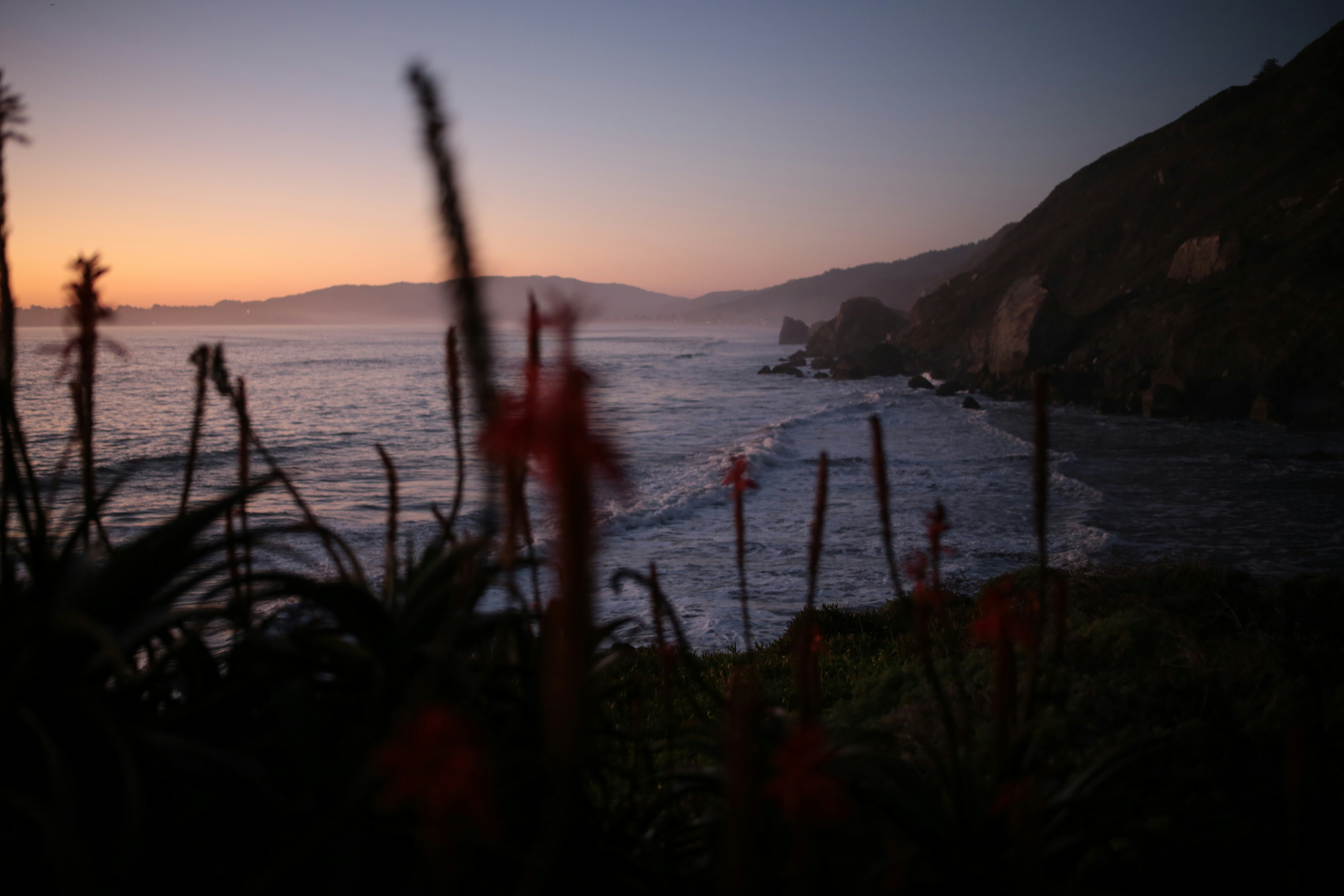 Coastal landscape at dusk with ocean and hills.