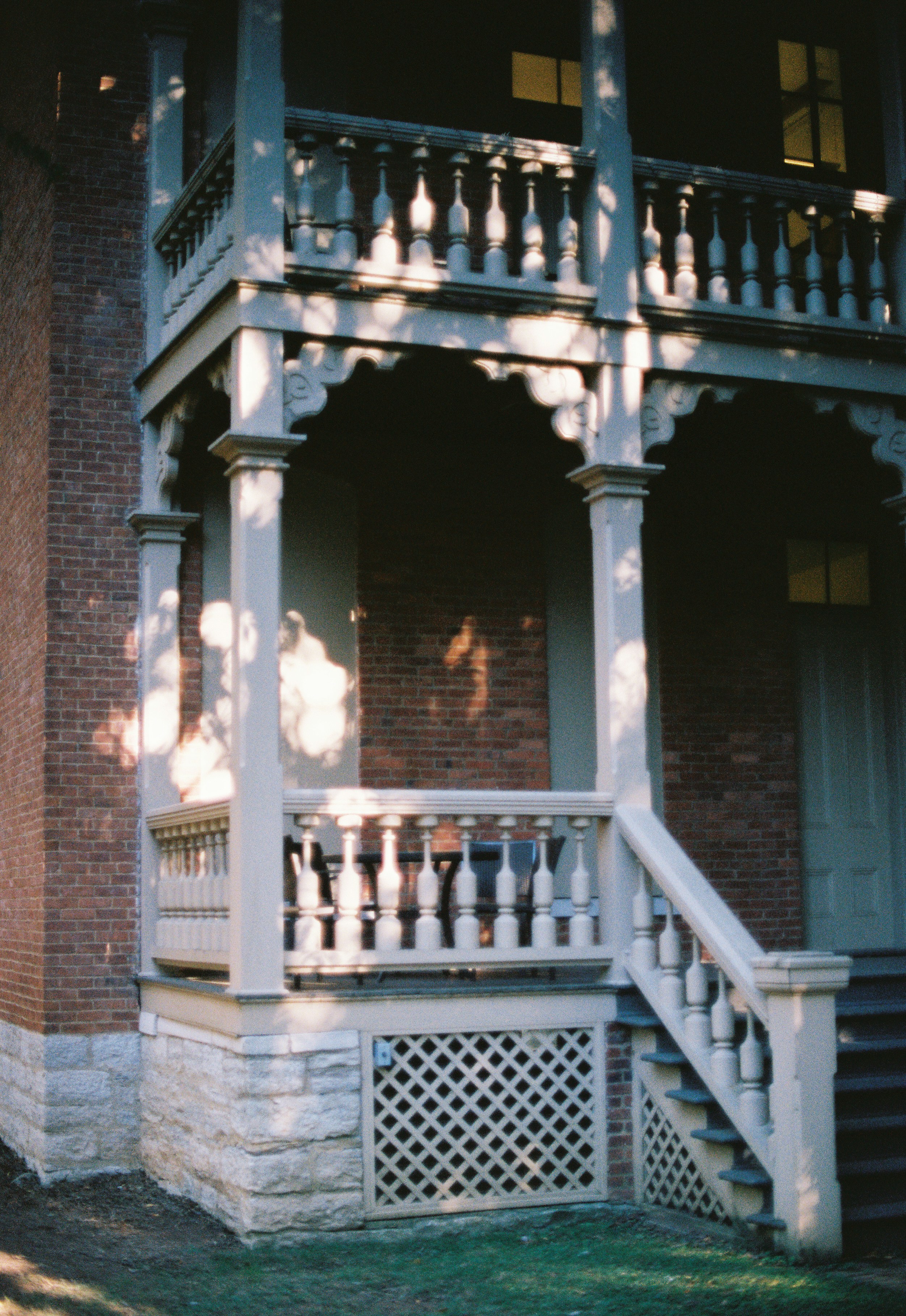 Ornate wooden porch with brick building and stone walls.