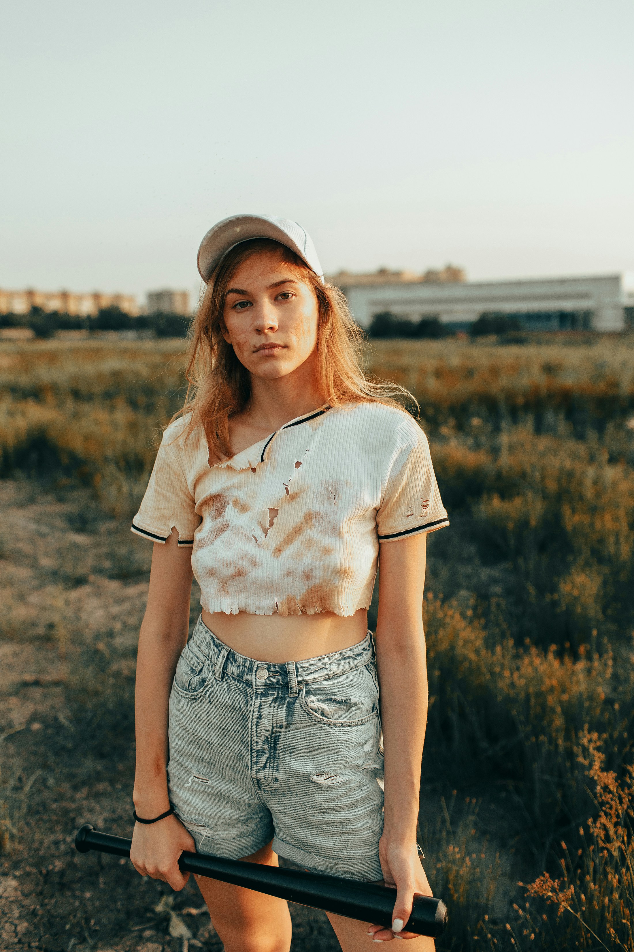 Young woman in cap and shorts holding baseball bat