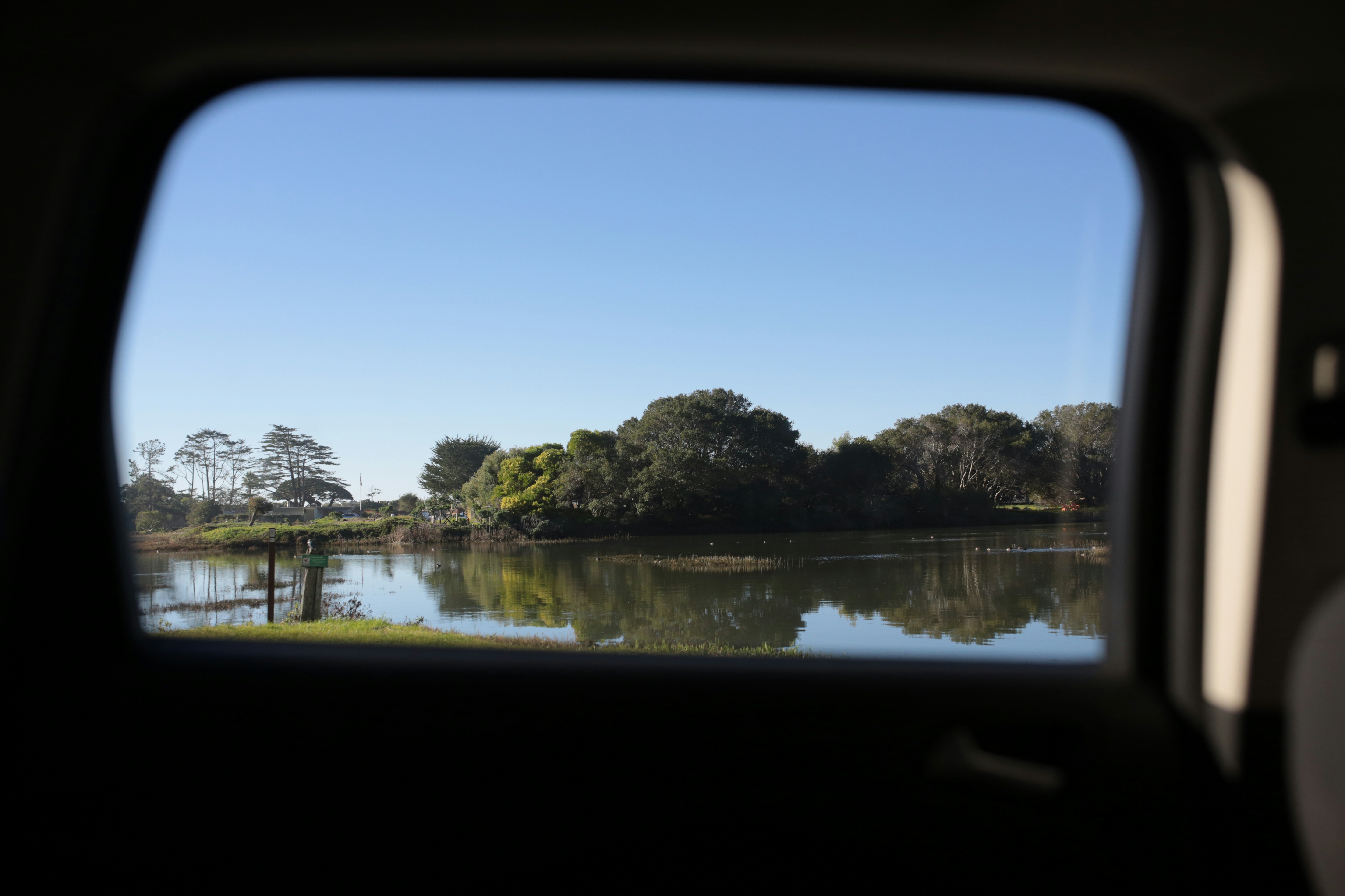 Calm lake reflects trees under a clear blue sky.
