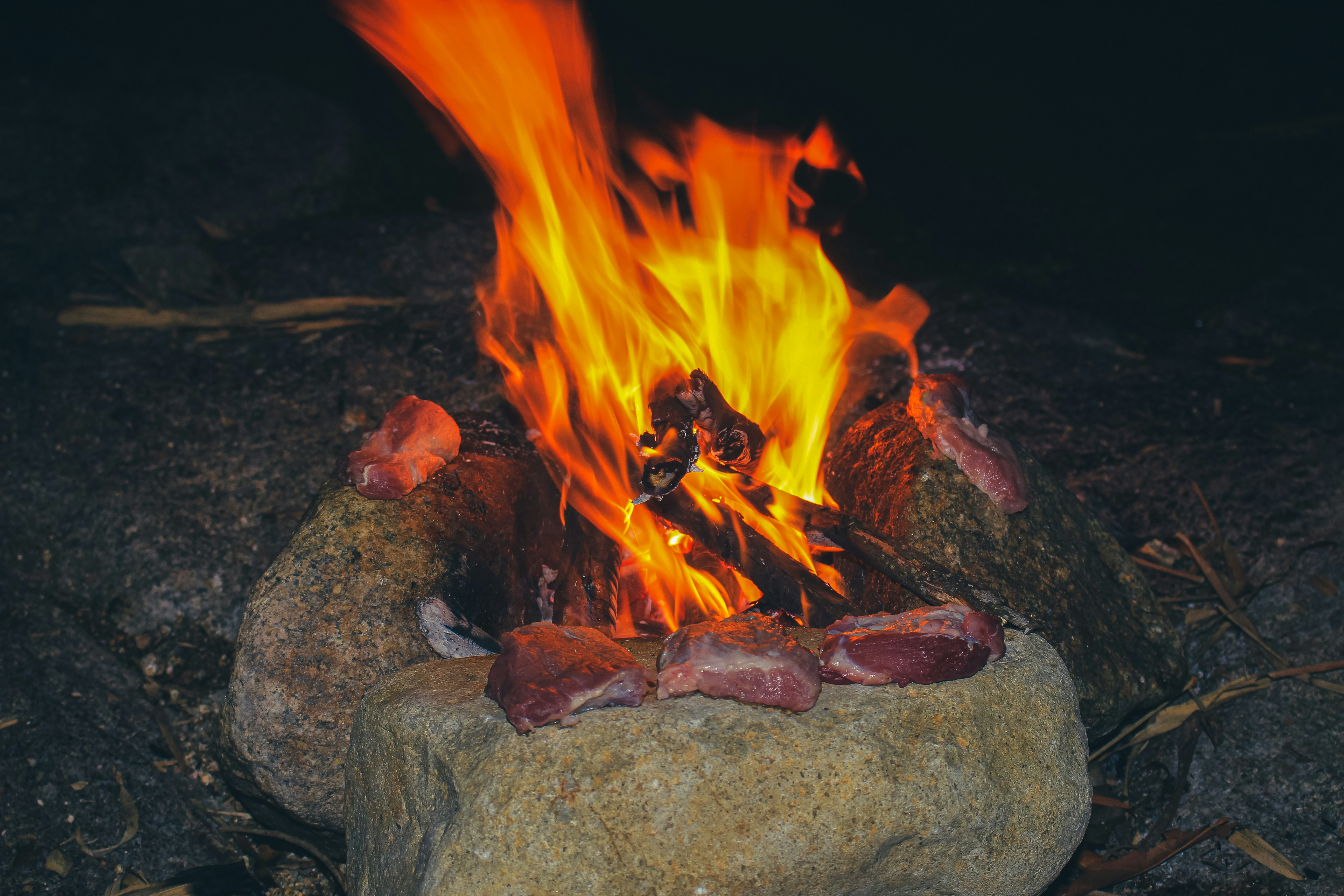 Raw meat cooking over a campfire at night