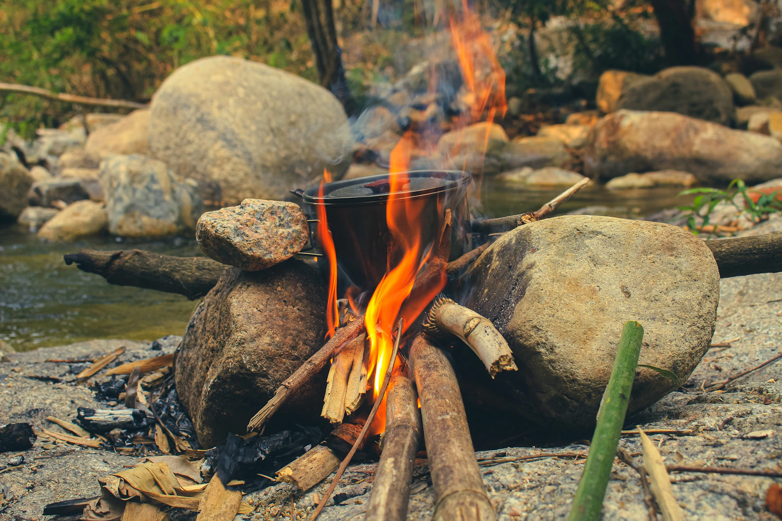 Cooking pot over an outdoor campfire beside a rocky stream