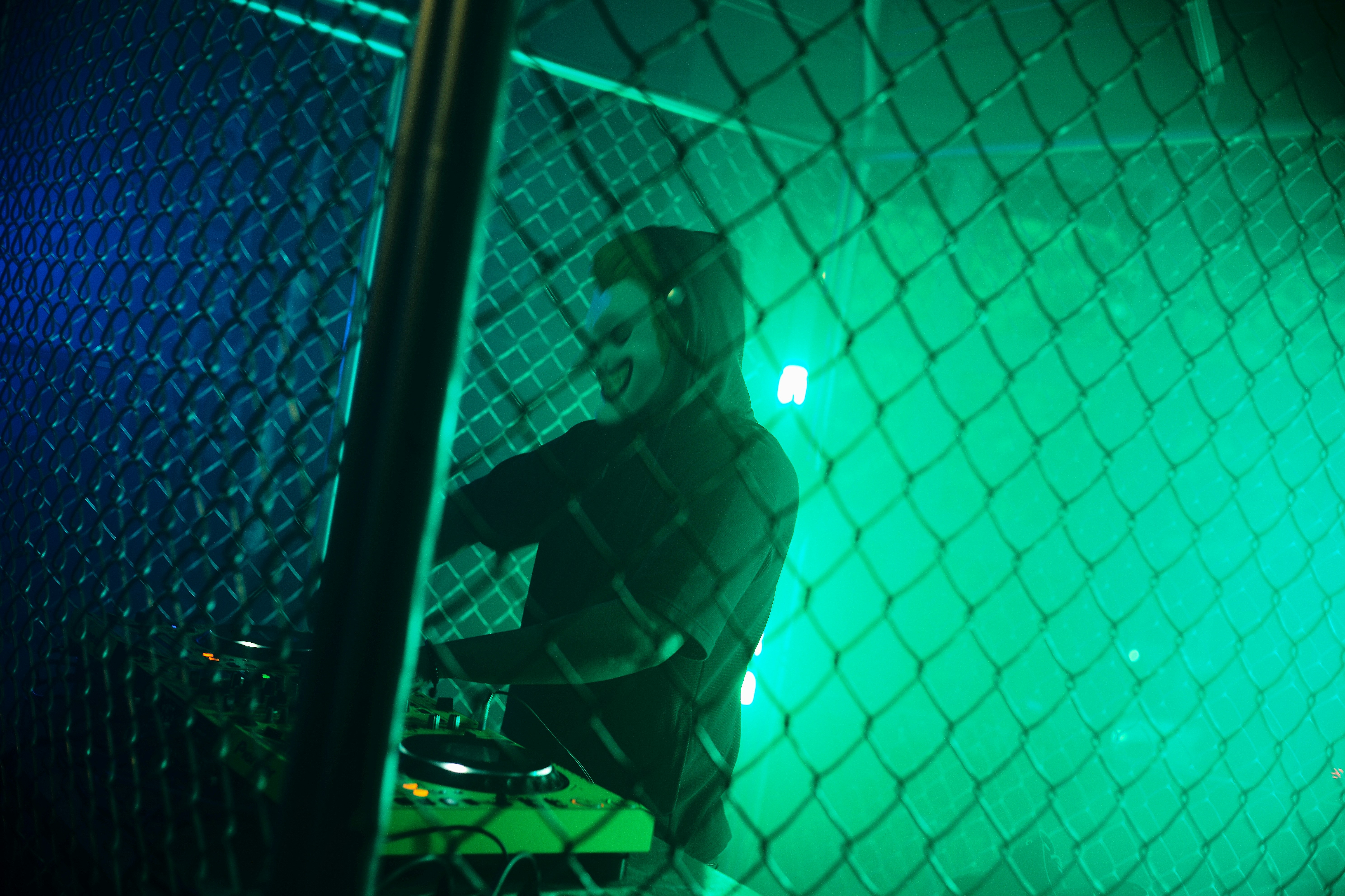 DJ performing behind a chain-link fence with green lights