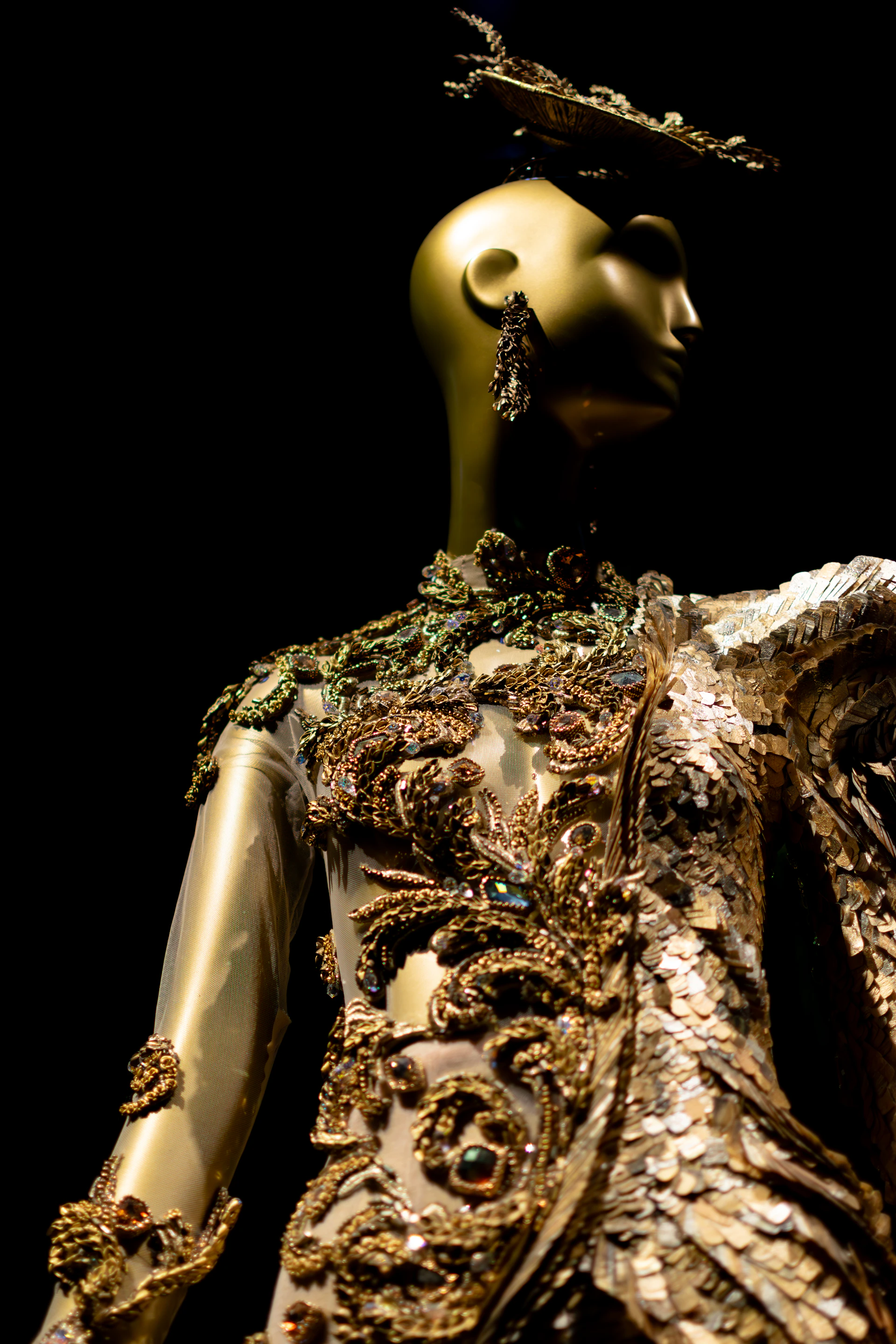 A golden mannequin wearing an ornate, sequined gown.