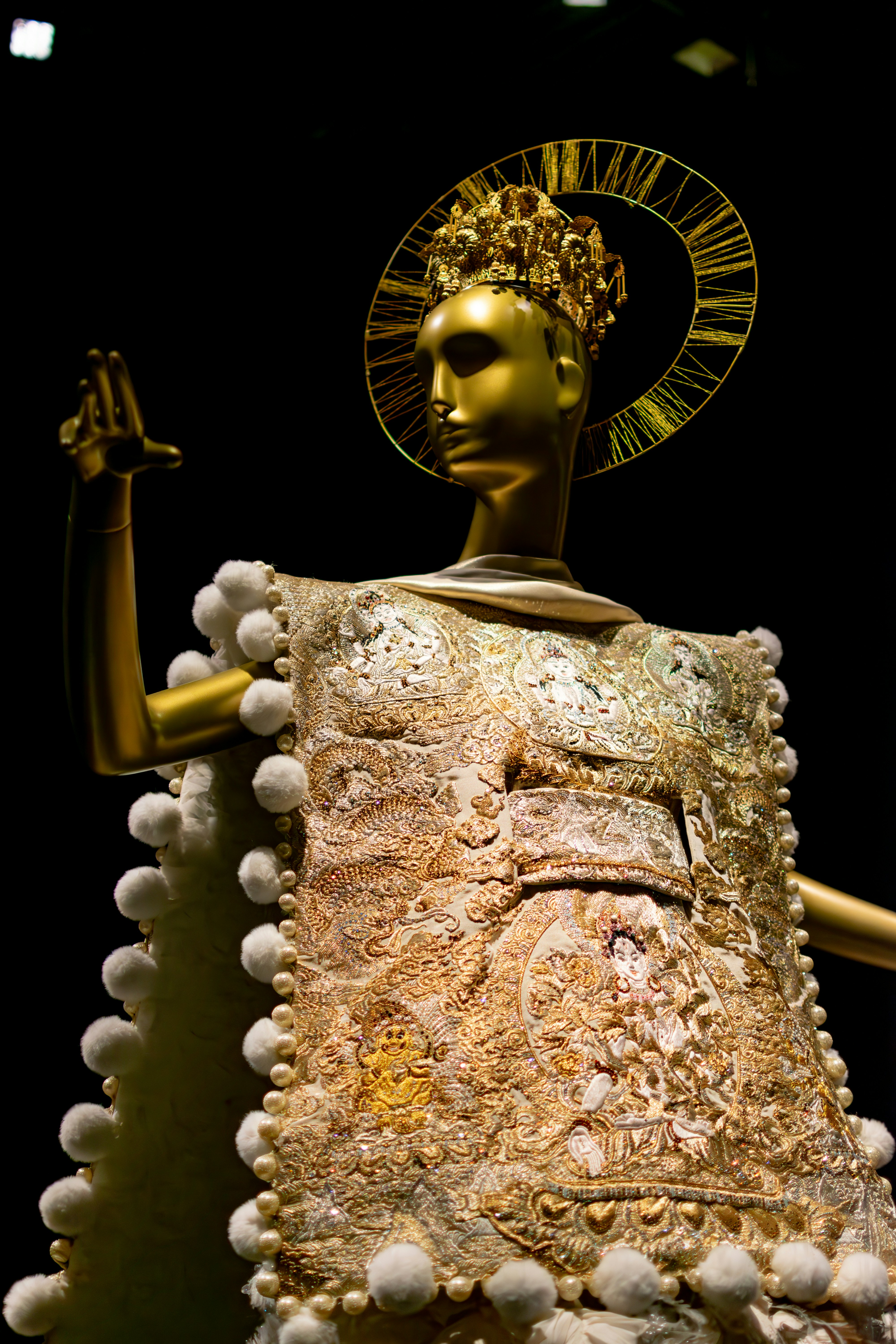 Golden mannequin in ornate, bejeweled ceremonial attire with halo.